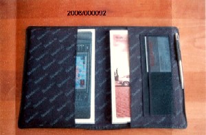Warenzusammenstellung, bestehend aus einem
Behältnis zur Aufnahme von KFZ-Papieren :
- aus Leder gearbeitet,
- an der Innenseite mit Spinnstoffen (Nylon) verkleidet,
- mit mehreren Einsteckfächern für Papiere und Visitenkarten ausgestattet,
- mit einer Lasche aus Leder als Halterung für einen Kugelschreiber versehen,
und einem Kugelschreiber :
- aus Stahl mit Firmenlogo bedruckt.

Einband aus Leder im Hinblick auf die Verwendung charakterbestimmend.