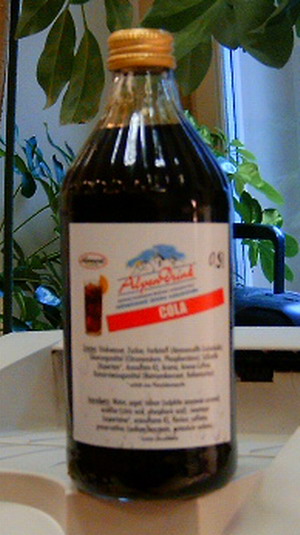 Dunkelbrauner, klarer, nach Cola riechender, nicht unmittelbar trinkbarer, nicht alkoholhaltiger aromatisierter Zuckersirup; im Wesentlichen bestehend aus Wasser, Zucker, Farbstoff (Ammonsulfit-Zuckerkulör), Säuerungsmittel (Citronensäure, Phosphorsäure), Süßstoffen (Aspartam, Acesulfam-K), Aroma, Coffein und Konservierungsmittel (Natriumbenzoat, Kaliumsorbat); dient mittels Verdünnen mit Wasser zur Herstellung eines Getränkes; 
aufgemacht in einer weißen, etikettierten Glasflasche, mit Metallschraubverschluss zu 0,5 Liter.