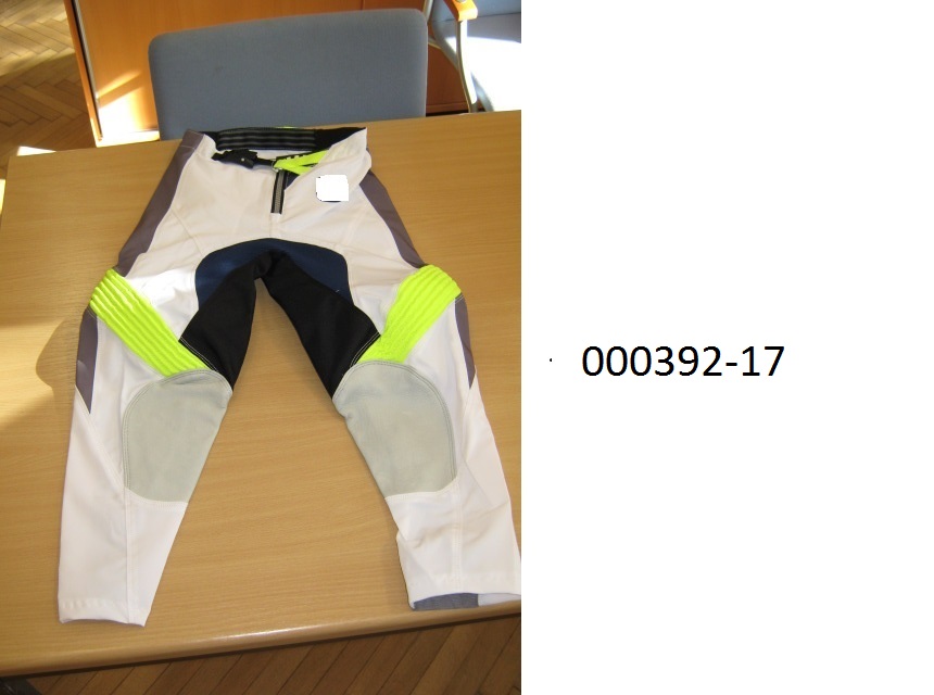 lange Hose (Motorradhose)
- beide Beine einzeln umschließend und bis zu den Knöcheln reichend,
- mittels Zippverschluss vorne verschließbar,
- verarbeitet mit einer im Bund integrierten Gürtelschnalle, links über rechts verschließbar (für Männer oder Knaben), 
- gefüttert mit einer netzartigen Wirkware,
- bestehend aus patchworkartig zusammengenähten Gewirken und Geweben aus synthetischen Spinnstoffen auf Polyesterbasis, welche auf der Rückseite teilweise mit einer Folie auf PUR-Basis beschichtet sind (mit freiem Auge erkennbar), die nicht beschichteten Flächenerzeugnisse aus Gewebe überwiegen,
- im Innenseitenbereich der Unterschenkel mit eingenähten Lederteilen ausgestattet,
- im linken Unterschenkel mit einem Prallschutz in Form von zwei geschäumten, mit Spinnstoff überzogenen Kunststoffplatten verarbeitet,
- aufgrund der Verarbeitung als Motorradhose für Knaben erkennbar, keine Arbeits- oder Berufsbekleidung.
(Abbildung siehe Anlage)