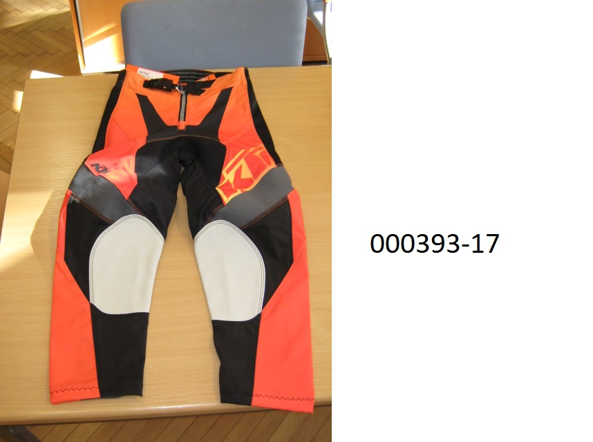 lange Hose (Motorradhose)
- beide Beine einzeln umschließend und bis zu den Knöcheln reichend,
- mittels Zippverschluss vorne verschließbar,
- verarbeitet mit einer im Bund integrierten Gürtelschnalle, links über rechts verschließbar (für Männer oder Knaben), 
- bestehend aus patchworkartig zusammengenähten, bedruckten Gewirken und Geweben aus synthetischen Spinnstoffen auf Polyesterbasis, das Gewebe überwiegt, 
- im Gesäßbereich rückseitig mit einer dünnen Schicht auf PUR-Basis (mit freiem Auge sichtbar) überzogen,
- im Kniebereich mit eingenähten Lederteilen ausgestattet,
- aufgrund der Verarbeitung als Motorradhose für Knaben erkennbar, keine Arbeits- oder Berufsbekleidung.
(Abbildung siehe Anlage)