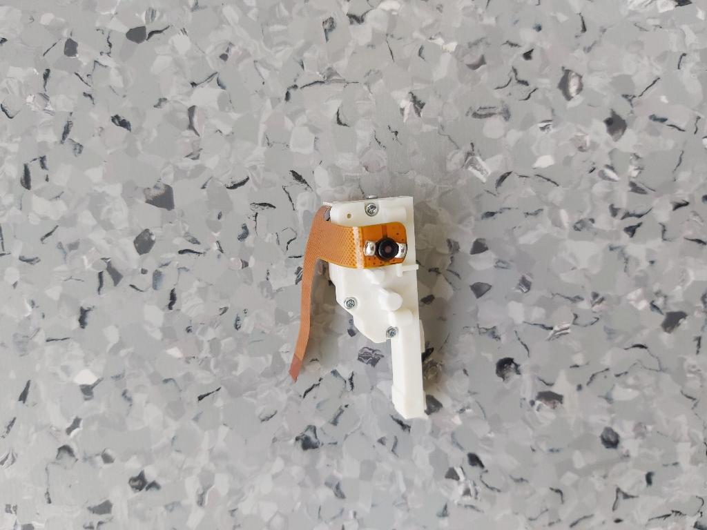 Elektrischer Linearantrieb,
- bestehend aus einem rotierenden Gleichstrommotor für eine Leistung von weniger als 37,5 Watt (5,0 VDC Nennspannung) und einem optischen Inkrementalgeber mit gemeinsamen Flachbandanschlusskabel, einem mehrstufigen Zahnradgetriebe und einem linear arbeitenden Stellglied (Zahnstange), montiert an einem mehrteiligen Kunststoffträger mit Montagevorrichtungen,
- nach Versorgen des Gleichstrommotors mit Nennspannung wird die Zahnstange je nach Polung ausgeschoben oder eingezogen,
- die Hublänge beträgt ca. 18 mm.
(Abbildung laut Anlage)