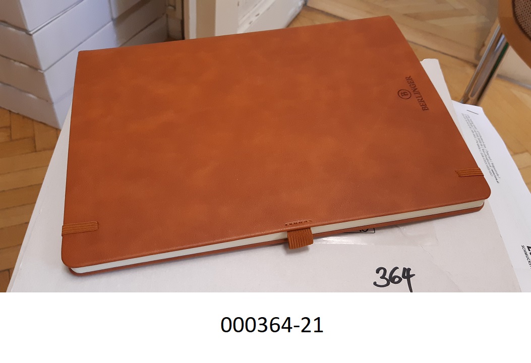 Notizbuch aus Papier
- mit den Maßen von ca. 21,4 x 28,7cm,
- gebunden, mit einem festen Einband aus einer mit Kunststoff umhüllter Pappe (mit Ausnahme des Rückens), welcher auf den Außenseiten mit Schaumkunststoff gepolstert und mit lederartig geprägter Kunststofffolie überzogen ist,
- mit Blättern, welche auf den ersten beiden Seiten beidseitig vollständig liniert bedruckt, danach glatt ausgeführt sind,
- mit einem am Buchrücken angebrachten Band aus Spinnstoffen als Lesezeichen,
- mit einem elastischen Band zum Verschließen des Blockes und einer elastischen Schlaufe für ein Schreibgerät ausgestattet,
- ohne Kalendarium.
 (Abbildung siehe Anlage)