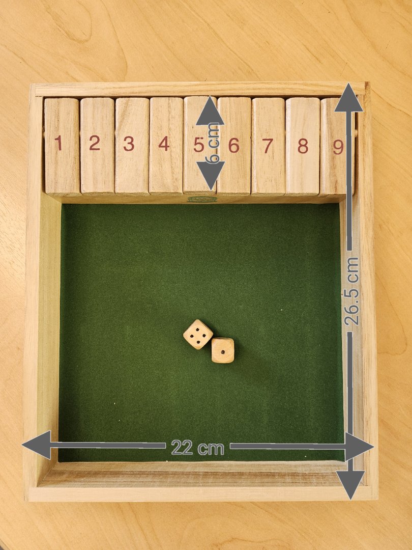 Gesellschaftsspiel in Form eines Würfelspieles, 
- bestehend aus einem ca. 26,5 x 22cm großen Holzkistchen, dessen Boden innen mit Textil ausgelegt ist,
- an einer Breitseite befinden sich neun hochklappbare Holzklötzchen, die beidseitig mit den Ziffern von 1 – 9 bedruckt sind,
- mit zwei Würfeln aus Holz – jeweils mit 1 bis 6 Punkten bedruckt – ausgestattet,
- Ziel des Spiels ist es, möglichst viele oder alle Ziffern durch entsprechendes Würfeln der Zahlen zuzuklappen.
Laut Antragsteller stammt das Holz vom Blauglocken-Baum (Paulownia Holz).
(Abbildung siehe Anlage)