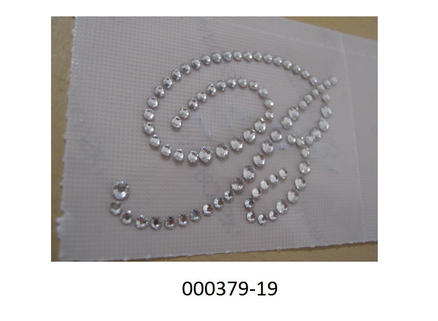 Edelsteinnachbildung aus Glas
- als Motiv (in Form eines Schönschrift B) auf einer Kunststofffolie angeordnet,
- von runder Form mit scharfkantigen Flächen, mit thermoplastischer Rückseite (auf Polyamidbasis), keine Einfassung,
- geschliffen und mechanisch poliert,
- auf der Vorder- und Rückseite mit einer Schutzfolie abgedeckt,
- laut Hersteller Verwendung in der Textilindustrie (kann auf Stoff aufgebügelt werden).
(Abbildung siehe Anlage)