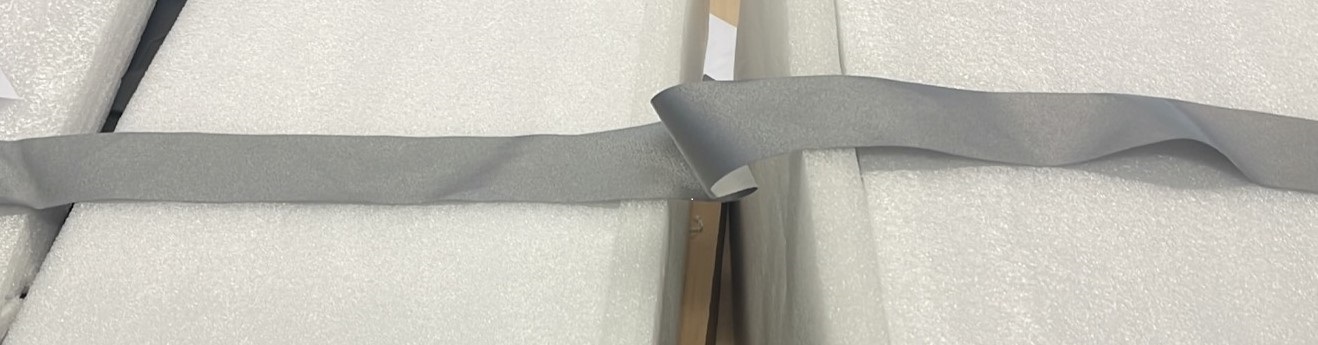 Een strook weefsel van ongeveer 5 cm breed met een grijze, reflecterende deklaag. Het weefsel bestaat uit garens van hoofdzakelijk polyester en in minder mate uit katoen. De deklaag is samengesteld uit acryllijm waarin met microscopie kleine bolletjes te zien zijn.