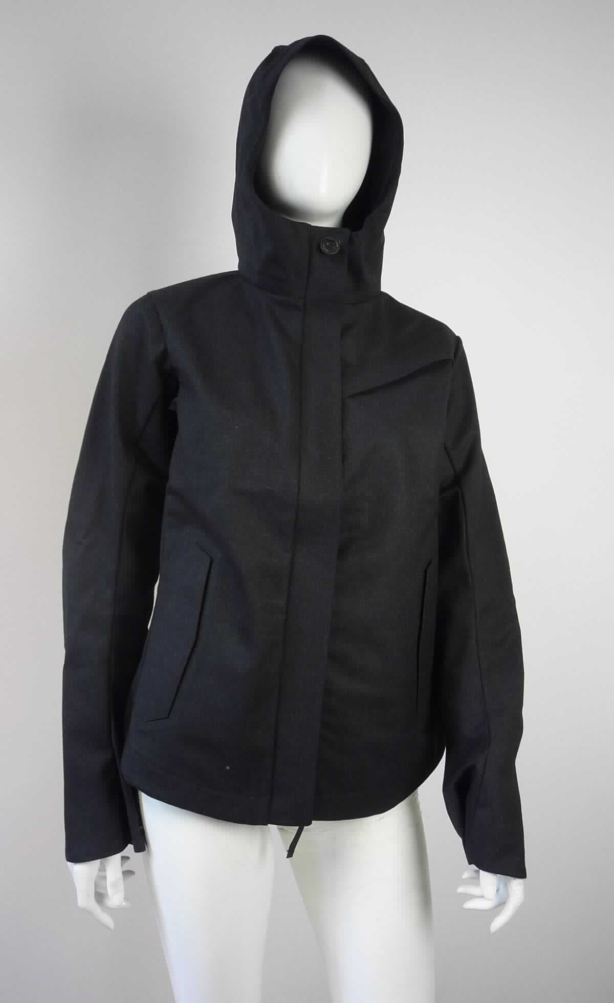 Anorakähnliches Kleidungsstück, sog. Jacket hardshell AKSLA / bonded, Art. 820101, Größe S, Foto siehe Anlage,
- aus einem ca. 0,6 mm dicken, dreilagigen Flächenerzeugnis mit einer Außenlage aus buntgewebten Geweben 
  (melierte Garne), einer Zwischenlage aus einer Kunststofffolie (laut Antrag aus Polyurethan; kein Zellkunststoff), 
  die im Querschnitt mit bloßem Auge nicht wahrnehmbar ist (keine Meterware der Position 5903), und einer 
  Innenlage aus einfarbigen Gewirken; beide Flächenerzeugnisse laut Antrag (überwiegend) aus Schurwolle sowie
  Polyester und Elasthan (beides synthetische Chemiefasern),
- über die Taille reichend (Rückenlänge: ca. 57 cm), vorn ca. 7 cm länger und abgerundet gearbeitet,
- mit einer Kapuze,
- vorn mit einer durchgehenden Öffnung mit Reißverschluss, verdeckt durch eine Patte mit Knopfverschluss
  von rechts über links (Frauenkleidung),
- mit langen Ärmeln, an den Ärmelenden mit Druckknöpfen zu verengen,
- an den Unterseiten der Ärmel mit Öffnungen,
- vorn mit einer Brusttasche und zwei eingesetzten Taschen unterhalb der Taille, alle mit Reißverschluss und Patte, 
- am unteren Rand durch Umschlagen und Festnähen gesäumt,
- wird im Allgemeinen über jeder anderen Kleidung und zum Schutz gegen das Wetter getragen,
- insbesondere im Hinblick auf das äußere Erscheinungsbild sind die die Außenlage bildenden Gewebe charakter-
  bestimmend.

"Anorakähnliches Kleidungsstück, aus Geweben, für Frauen, aus Wolle"