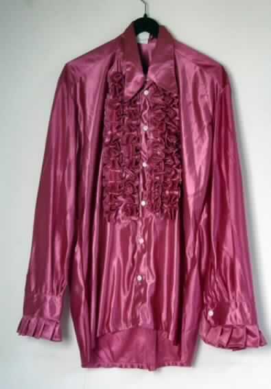 Hemd für Männer, sog. Disco Shirt pink, Art. 86885, Größe 52, Foto siehe Anlage
- aus 0,3 mm dicken, einfarbigen Gewirken aus laut Antrag 100 % synthetischen Chemiefasern, in jeder 
  Richtung mit durchschnittlich mehr als 10 Maschen je linearen Zentimeter,
- mit einem halsnahen Umlegekragen,
- vorn mit einer durchgehenden Öffnung von links über rechts geknöpft (Männerkleidung), 
- mit langen Ärmeln, mit manschettenartigen Abschlüssen, 
- beiderseits der Öffnung und an den Ärmelabschlüssen mit angenähten, gerüschten Gewirkezuschnitten verziert,
- über den Schritt, aber nicht über den halben Oberschenkel reichend (Rückenlänge: 88 cm),
- am unteren Rand gesäumt,
- gehört als Maskenkostüm aus Spinnstoffen nicht zum Warenkreis der Position 9505.

"Hemd aus Gewirken, für Männer, aus synthetischen Chemiefasern"
