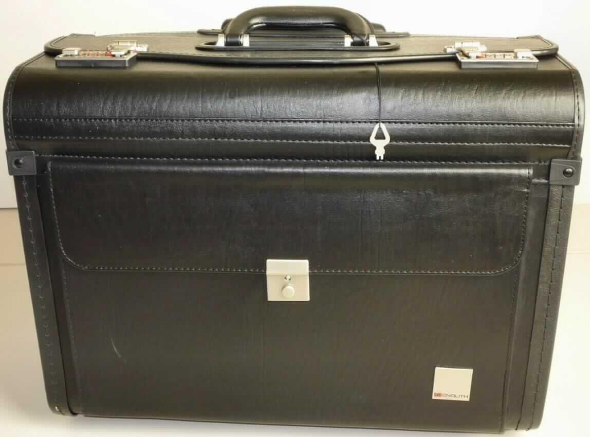 Aktenkoffer, sog. schwarzer Pilotenkoffer mit Trolleysystem und Laptopfach, Foto siehe Anlage,
- mit einer Außenseite aus Kunststofffolien (lederartig geprägt),
- mit formstabilisierender Unterlage,
- in den Abmessungen: ca. 38 cm (Höhe) x 48 cm (Breite) x 25 cm (Tiefe),
- mit einem Bügeltragegriff und zwei Zahlenschlössern mit Schnappverschluss,
- mit einem ausziehbaren Griff aus Kunststoff mit Gestänge aus Metall zum Ziehen (Trolley),
- mit zwei Rollen aus Kunststoff,
- mit zwei Standfüßen aus mit Kunststoff überzogenem Metall,
- auf der Vorderseite mit einem aufgesetzten Vorfach mit Überschlagklappe mit Schnappverschluss und Schloss,
- auf beiden Schmalseiten mit einer Außentasche mit Überschlagklappe mit Klettverschluss, 
- Deckel zweiteilig zu öffnen,
- auf der Innenseite des Deckels mit einem aufgesetzten Reißverschlussfach und drei Stiftlaschen versehen,
- ein großes Hauptfach, auf einer Seite mit einem Aktenfach mit Dehnfalte, auf der anderen Seite mit einem
  gepolsterten Laptopfach mit einem Klettriegel,
- gefüttert.

"Aktenkoffer, mit Außenseite aus Kunststofffolien"
