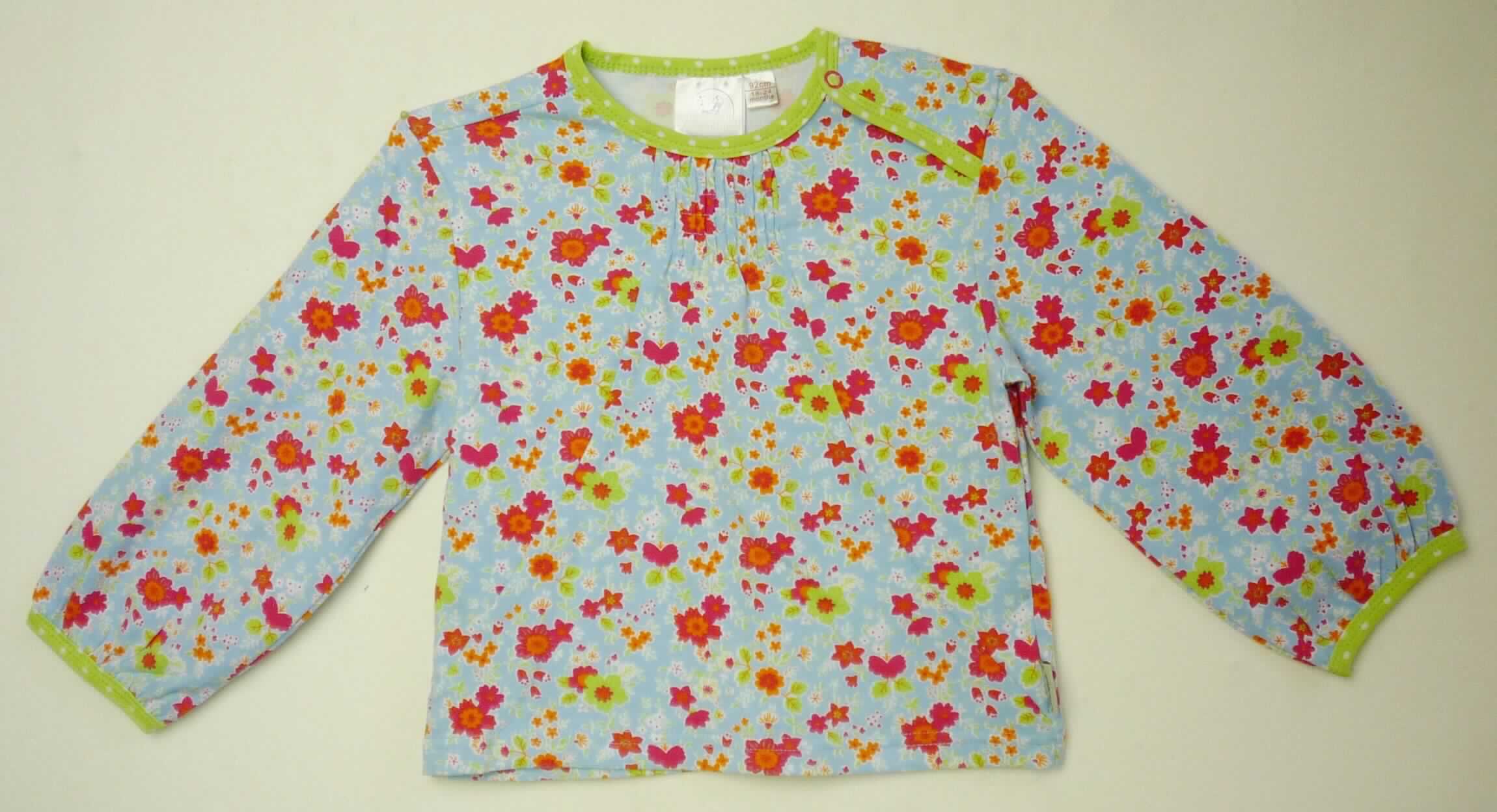 Bluse, sog. Shirt (unisex), Art. 2801625, Größe 92, Foto siehe Anlage,
- aus ca. 0,6 mm dicken (leichten), bedruckten Gewirken aus laut Antrag 95 % Baumwolle und 5 % Elasthan 
  (synthetische Chemiefasern), mit mehr als 10 Maschen je linearen Zentimeter in jeder Richtung,
- bis über die Taille reichend (Rückenlänge ca. 34 cm),
- mit einem runden Halsausschnitt mit kontrastfarbener Randeinfassung,
- auf einer Schulter mit einer kurzen Öffnung mit Druckknopfverschluss (somit kein T-Shirt oder modisches 
  Unterhemd),
- ohne Hinweise auf den Trägerkreis (unisex),
- mit langen Ärmeln, an den Ärmelenden mit Gewirkebändern eingefasst und verengt,
- vorn unterhalb des Halsausschnitts teilweise elastisch gerafft,
- am unteren Rand durch Umschlagen und Festnähen gesäumt.

"Bluse, aus Gewirken, für Mädchen, aus Baumwolle"