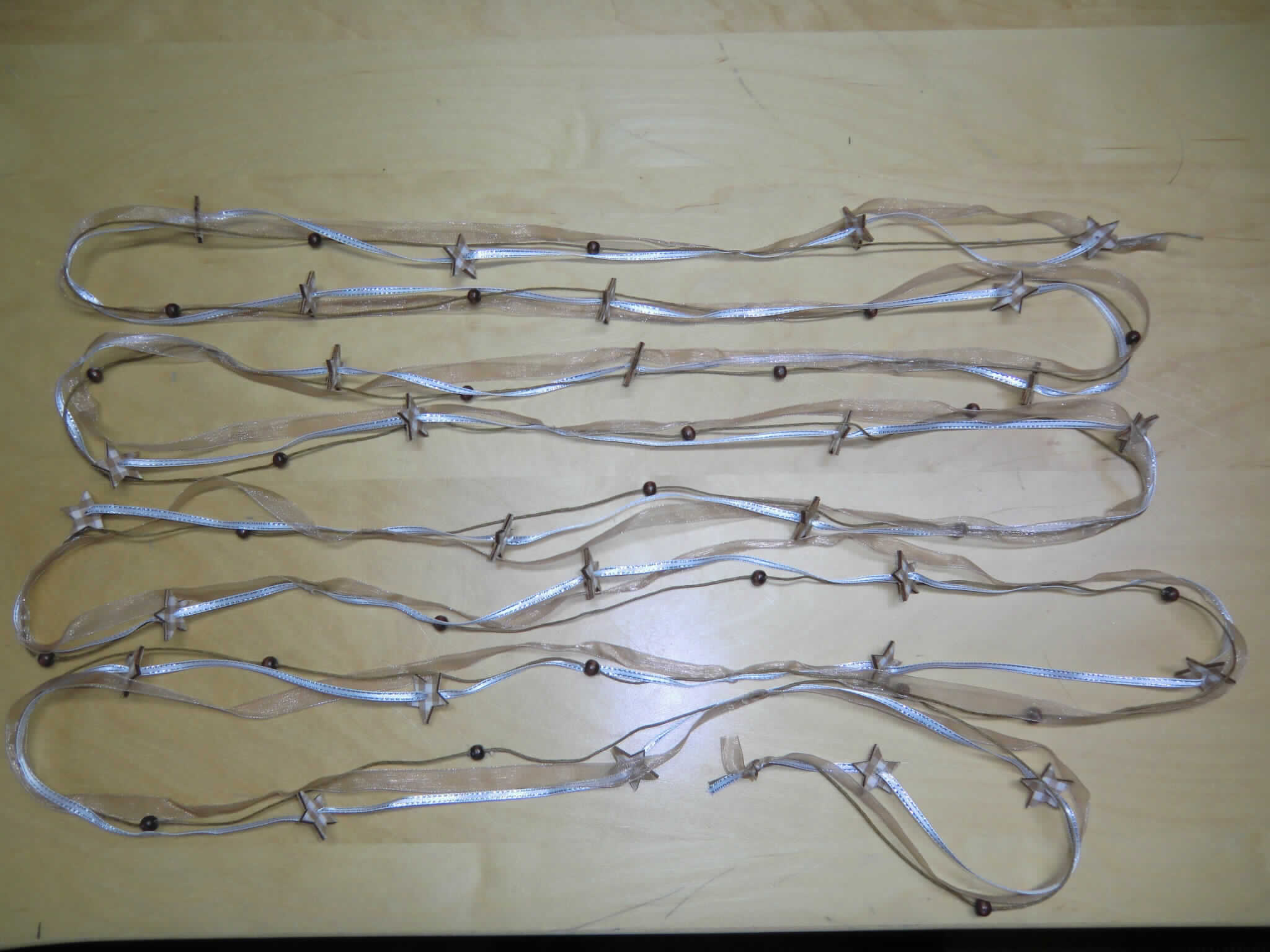 Posamentierware, sog. Geschenkband mit Sternen braun/silber, Artikel 60388, Fotos siehe Anlage,
- Ware mit Meterwarencharakter; laut Antrag mit einer Länge von 5 m,
- aus drei, in regelmäßigen Abständen (laut Antrag: 32 cm) miteinander verklebten, verschiedenen Strängen
  (weiß/silberfarbenes Band, braunes Band, Bindfaden); an den Enden nicht eingefasst,
-- weiß/silberfarbenes Band:
--- aus buntgewebtem (weiß/siberfarbenem) Gewebe aus laut Antrag Polyester (synthetische Chemiefasern)
    und metallisierten Garnen aus laut Antrag aus Polyester (synthetische Spinnmasse),
--- mit einer Breite von etwa 4 mm,
--- mit aufgefädelten, flachen Sternen aus laut Antrag Sperrholz; mit Gewebe überzogen,
-- braunes Band:
--- einfarbiges (braunes) Gewebe aus laut Antrag Polyester (synthetische Chemiefasern),
--- mit einer Breite von etwa 1 cm,
-- Rundgeflecht:
--- aus laut Antrag Hanf,
--- mit einem Durchmesser von etwa 1,1 mm,
--- mit aufgefädelten Perlen aus laut Antrag Pinienholz.

"Posamentierware, als Meterware, ohne Stickerei, nicht aus Gewirken oder Gestricken"
