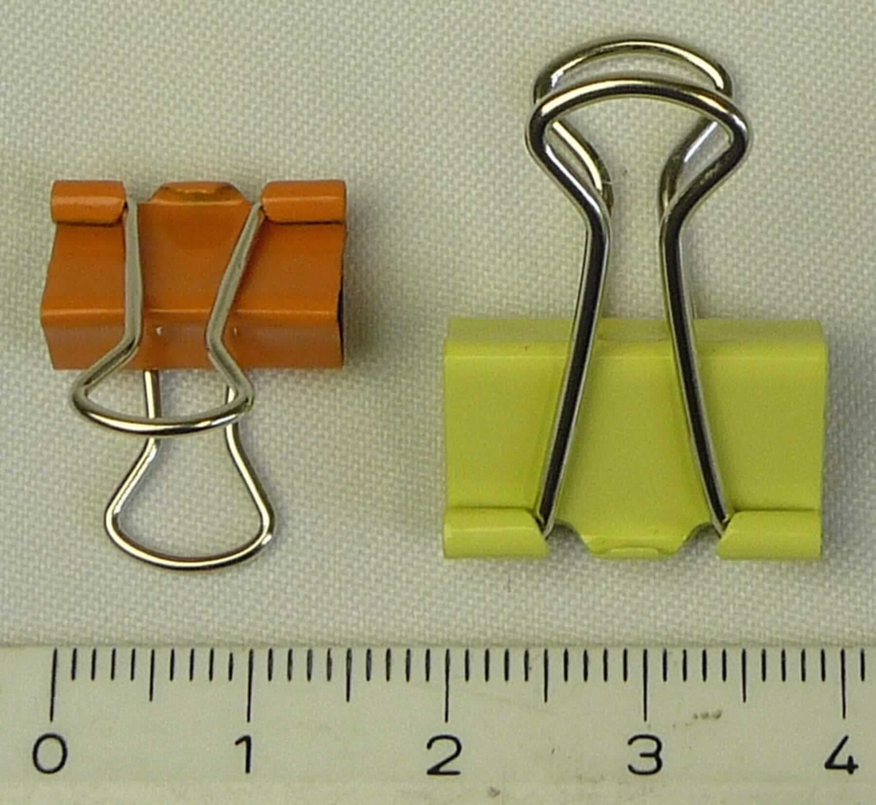 Es handelt sich um aus unedlem Metall gefertigte Klemmvorrichtungen aus einem etwa 15 mm bzw, 19 mm breiten Blechzuschnitt, der zu einem geraden Prisma gebogen ist. An der Spitze des Prismas sind zwei aus Draht gebogenen Bügel beweglich befestigt, mit denen die unter Spannung stehende Klammer geöffnet werden kann. Die Erzeugnisse dienen zum Zusammenhalten von z. B. Papierseiten.

Abbildung siehe Anlage.

Derartige Erzeugnisse gehören als "den Briefklammern und Aktenklammern ähnliches Büromaterial aus unedlen Metallen" zum TARIC-Code 8305 9000 00.