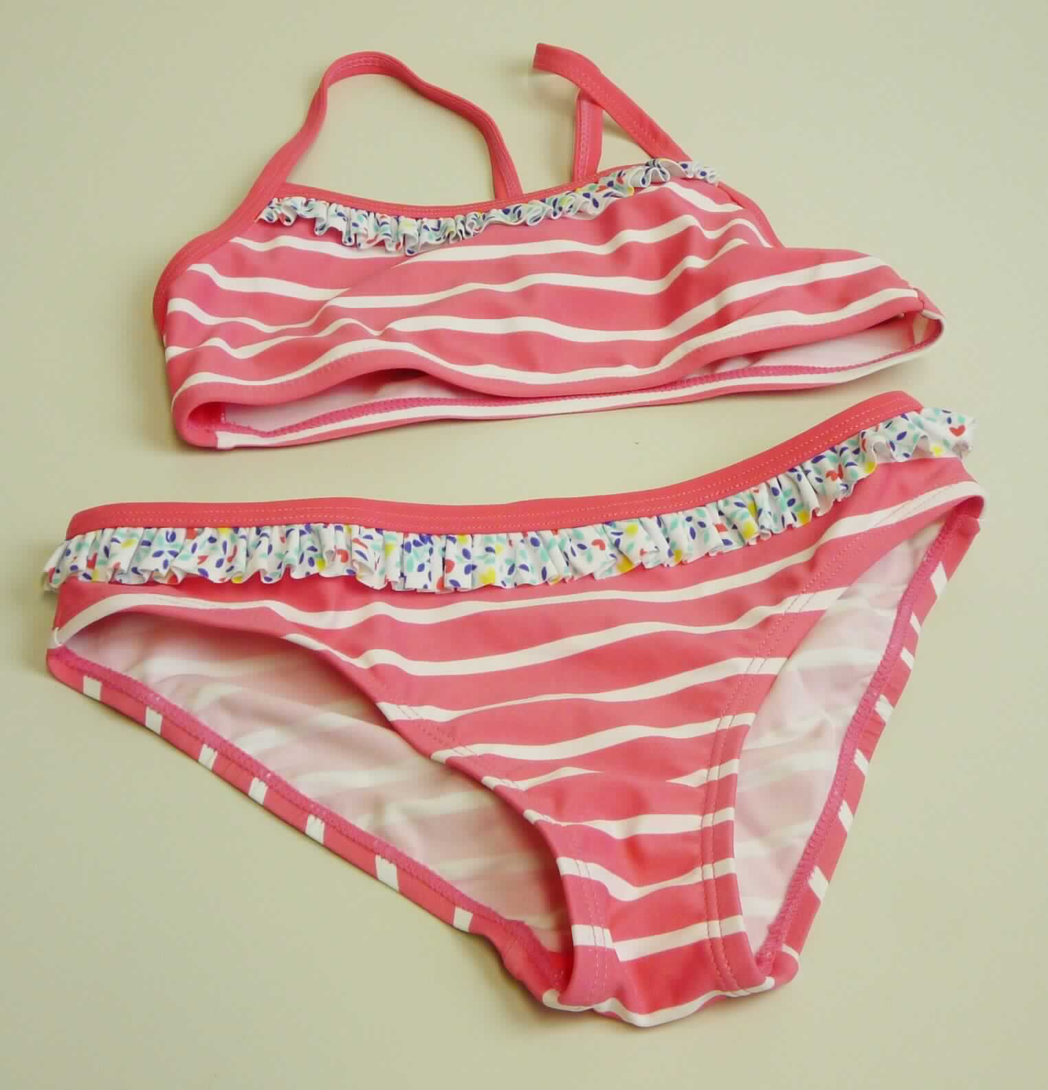 Zweiteiliger Badeanzug, sog. Mädchen Bustier-Bikini, Art. 155998, Farbe 504-pink, Größe 128, Foto siehe Anlage,
- in einem Polybeutel verpackt,
- aus 0,5 mm dicken, bedruckten Gewirken aus laut Antrag 80 % Polyamid und 20 % Elasthan (Elastomergarn,
  beides synthetische Chemiefasern); ohne Kautschukfäden,
- Oberteil:
-- in Art eines Büstenhalters gearbeitet,
-- ohne Öffnung und ohne Verschluss,
-- die Brust bedeckend, 
-- mit Spaghettiträgern,
-- vorn dünn unterlegt,
- Unterteil:
-- in Form eines Hüftslips gearbeitet,
-- in der Taille abschließend,
-- vorn und im Schrittbereich mit einem Gewirke unterlegt (Hygieneeinlage),
-- mit hohen Beinausschnitten,
- mit gerüscht aufgenähten, schmalen Zuschnitten aus bedruckten Gewirken verziert,
- an den Rändern mit eingenähten, elastischen Bändern ausgestattet,
- aufgrund des Schnitts und der Ausstattung als Mädchenkleidung erkennbar,
- nach Schnitt, Material und Ausstattung erkennbar dazu bestimmt, als Badekleidung getragen zu werden.

"Badeanzug, aus Gewirken, für Mädchen, aus synthetischen Chemiefasern, ohne Kautschukfäden"