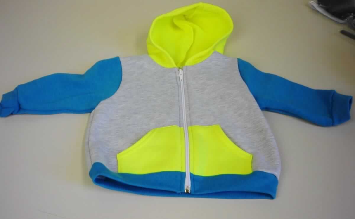 Blouson, sog. Strick Poly Hoody, Art. F097, für Kinder von 1-2 Jahren (entspricht Größe 86/92), Foto siehe Anlage,
- aus verschiedenen, ca. 1,8 mm dicken, einfarbigen und buntgewirkten, einseitig (Innenseite) gerauten Gewirken 
  (melierte Garne) aus laut Antrag 50 % Polyester (synthetische Chemiefasern) und 50 % Baumwolle,
- über die Taille reichend (Rückenlänge: ca. 33 cm),
- mit einer Kapuze,
- vorn mit einer durchgehenden Öffnung mit Reißverschluss,
- ohne Hinweise auf den Trägerkreis (unisex),
- mit langen Ärmeln, die über den unteren Rand des Kleidungsstücks hinausreichen; an den Ärmelenden
  mit angesetzten, verengenden Bündchen,
- mit zwei aufgesetzten Taschen (sog. Kängurutaschen) unterhalb der Taille,
- am unteren Rand mit einem angesetzten, verengenden Bund,
- aufgrund der Größe keine Kleidung für Kleinkinder der Position 6111.

"Blouson, aus Gewirken, für Mädchen, aus Chemiefasern"
