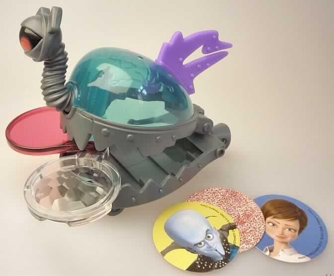 Bei dem "Lens Brainbot" aus der McDonald`s Aktion "Megamind 2010" handelt es sich um ein ca. 9 cm hohes und 11 cm langes Spielzeug aus Kunststoff, das ein Gehirn (durchscheinender farbiger Kunststoff) darstellen soll. Es ist mit einer Rolle zum Schieben ausgestattet und kann deckelartig geöffnet werden. Im Inneren befinden sich lose drei runde, beidseitig mit Gesichtern sowie verschlüsselten Bildern bedruckte Pappkarten und zwei ausschwenkbare Linsen. Mit Hilfe der Linsen können die Pappkarten-Bilder dechiffriert oder verzerrt (3D-Effekt) werden. 
Die Ware ist in einem Polybeutel für den Einzelverkauf aufgemacht und dient der spielerischen Unterhaltung von Kindern.

Sie ist als "anderes als zuvor von der Position 9503 erfasstes Spielzeug, aus Kunststoff" einzureihen.