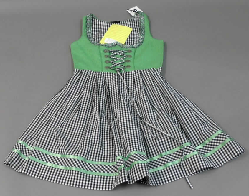 Dreiteilige Zusammenstellung bestehend aus einem Kleid, einem Oberteil (andere Kleidung) und einer Schürze, sog. Dirndl-Set, Order-Nr. 327493, Größe 36, Foto siehe Anlage,
- in Aufmachung für den Einzelverkauf,
- getrennte Einreihung der einzelnen Bestandteile, weil die Kleidungsstücke nicht als Kombination zusammen 
  in eine Position eingereiht werden dürfen, u.a. da das Kleid und die Schürze als Bestandteil einer Kombination 
  nicht zugelassen sind,
- Kleid:
-- aus ca. 0,3 mm dicken, buntgewebten Geweben bzw. aus ca. 0,8 mm dicken, einfarbigen, bestickten Geweben   
   (Meterware der Position 5810), lt. Antrag beides aus 100 % Baumwolle,
-- über den Schritt reichend (Rückenlänge: ca. 94 cm), kann aufgrund der Länge ohne ein weiteres, den
   Unterkörper bedeckendes Kleidungsstück als Kleid getragen werden,
-- oberhalb der Taille gefüttert,
-- mit einem annähernd runden, halsfernen Ausschnitt; am Rand mit einer aufgenähten Zierborte ausgestattet,
-- ohne Öffnung vorn; mit acht Zierösen bis zur Taille, durch die in Kreuzbindetechnik ein Bindeband
   eingezogen ist,
-- ohne Ärmel, mit weiten Armauschnitten,
-- seitlich mit einem Reißverschluss,
-- mit einem in der Taille angesetzten, in Falten gelegten Rockteil; mit zwei aufgenähten Zierbändern im Bereich
   des unteren Randes,
-- nicht nach dem Batikverfahren handbedruckt,
-- an allen Rändern gesäumt.

"Kleid aus Geweben und Stickereien, für Frauen, aus Baumwolle, nicht nach dem Batik-Verfahren handbedruckt"