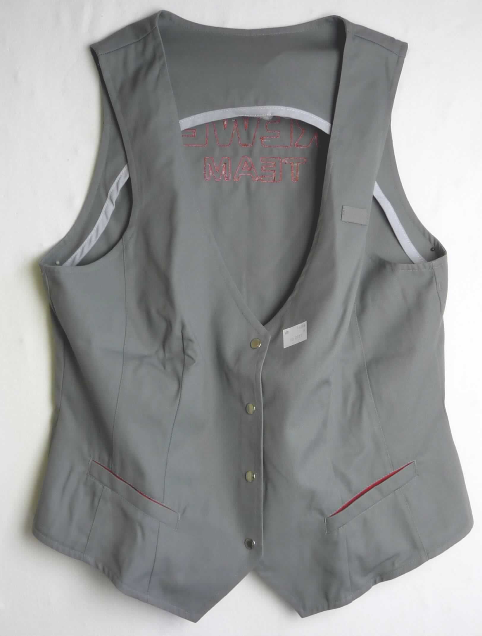Weste, sog. Damen Weste, Größe M, Foto siehe Anlage,
- aus ca. 0,4 mm dicken, einfarbigen Geweben aus laut Antrag aus 65 % Polyester (synthetische Chemiefasern)
  und 35 % Baumwolle,
- ungefüttert,
- über die Taille reichend (Rückenlänge: ca. 53 cm); mit spitz zulaufenden Vorderteilen, die ca. 7 cm länger 
  gearbeitet sind,
- mit einem V-förmigen Ausschnitt,
- vorn mit einer durchgehenden Öffnung mit Knopfverschluss von rechts auf links (Frauenkleidung),
- ärmellos, mit weiten Armausschnitten,
- vorn im Brustbereich mit einer Stiftlasche und zwei eingesetzten, offenen Taschen unterhalb der Taille, 
- hinten mit einem aufgestickten Firmenlogo, einer angenähten Riegelimitation und einer V-förmigen Aussparung
  am unteren Ende versehen,
- am unteren Rand gesäumt,
- lässt aufgrund seines allgemeinen Aussehens und der Beschaffenheit nicht erkennen, dass sie dazu bestimmt
  ist, ausschließlich oder hauptsächlich zum (körperlichen oder hygienischen) Schutz anderer Kleidungsstücke
  und/oder Personen bei Ausübung einer Gewerbe-,Berufs- oder Haushaltstätigkeit getragen zu werden, somit
  keine Arbeits- und Berufsbekleidung.

"Andere Kleidung (Weste), aus Geweben, für Frauen, aus Chemiefasern, keine Arbeits- und Berufskleidung"