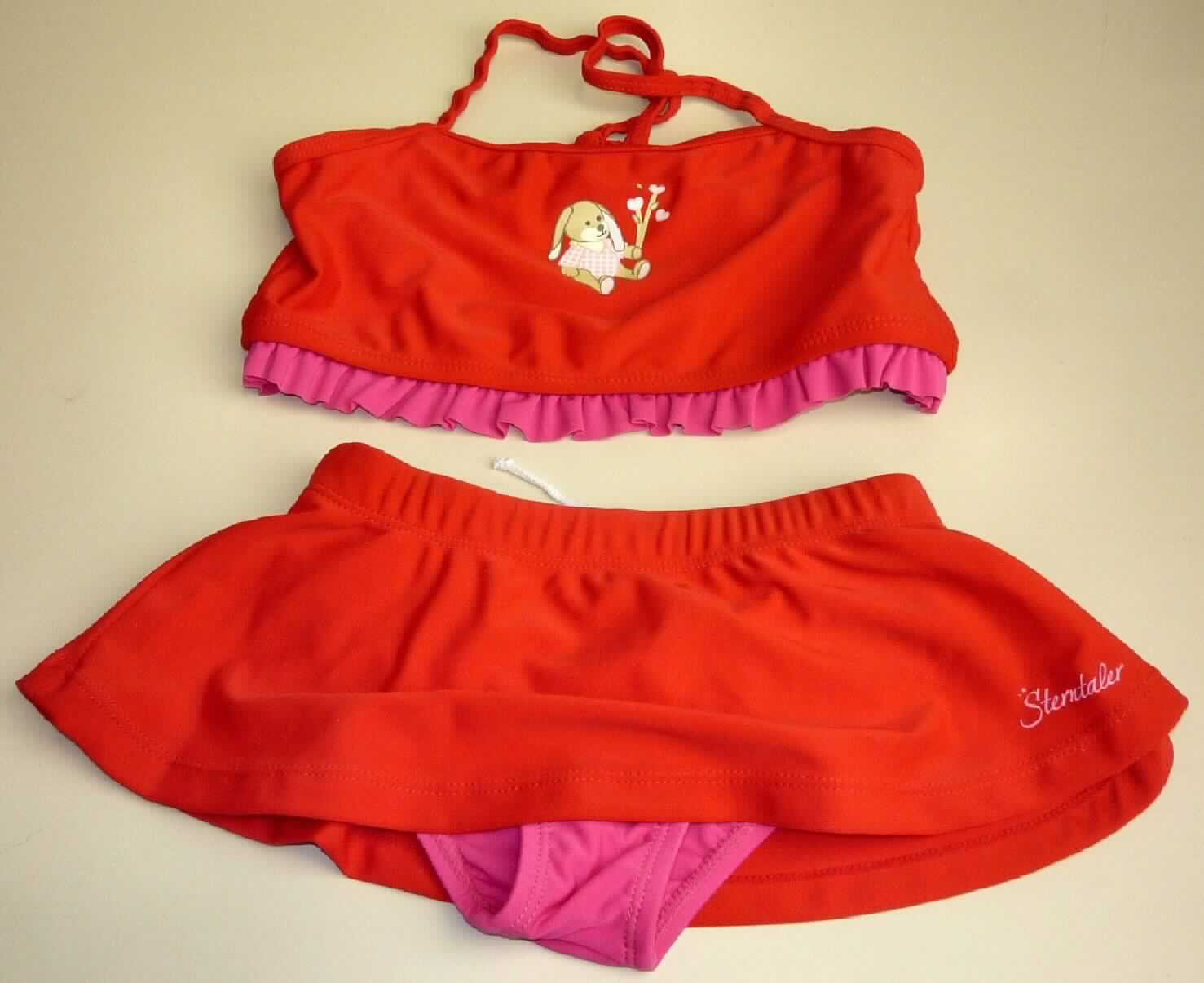 Zweiteiliger Badeanzug, sog. Bikini für Mädchen, Artikel 2521405, Größe 110/116, Foto siehe Anlage,
- aus verschiedenen, etwa 0,6 mm dicken, einfarbigen Gewirken aus laut Antrag 82% Polyamid und 18% Elasthan
  (Elastomergarn, beides synthetische Chemiefasern); ohne Kautschukfäden,
- Oberteil:
-- in der Art eines Bustiers gearbeitet,
-- die Brust bedeckend; vorn bedruckt, 
-- mit etwa 0,8 cm breiten Trägern (Spaghettiträger), 
-- ohne Öffnung und ohne Verschluss,
-- unterhalb der Brust mit einem elastischen Abschluss und einem angesetzten, gerüschten Volant,
- Unterteil:
-- in Form eines Taillenslips gearbeitet,
-- in der Taille abschließend; mit einem eingezogenen "Gummiband" und einem Kordelzug,
-- mit hohen Beinausschnitten; an den Rändern mit eingenähten, elastischen Bändern ausgestattet,
-- mit einem Schrittfutter (Hygieneeinlage),
-- mit einem am Bund angenähten, rockartigen, den Schritt nicht bedeckenden Überwurf,
- aufgrund des Schnitts und der Ausstattung als Mädchenkleidung erkennbar,
- die Kleidungsstücke lassen nach Schnitt, Material und Ausstattung erkennen, dass sie dazu bestimmt sind,
  als Badekleidung getragen zu werden.

"Badeanzug, aus Gewirken, für Mädchen, aus synthetischen Chemiefasern, ohne Kautschukfäden"