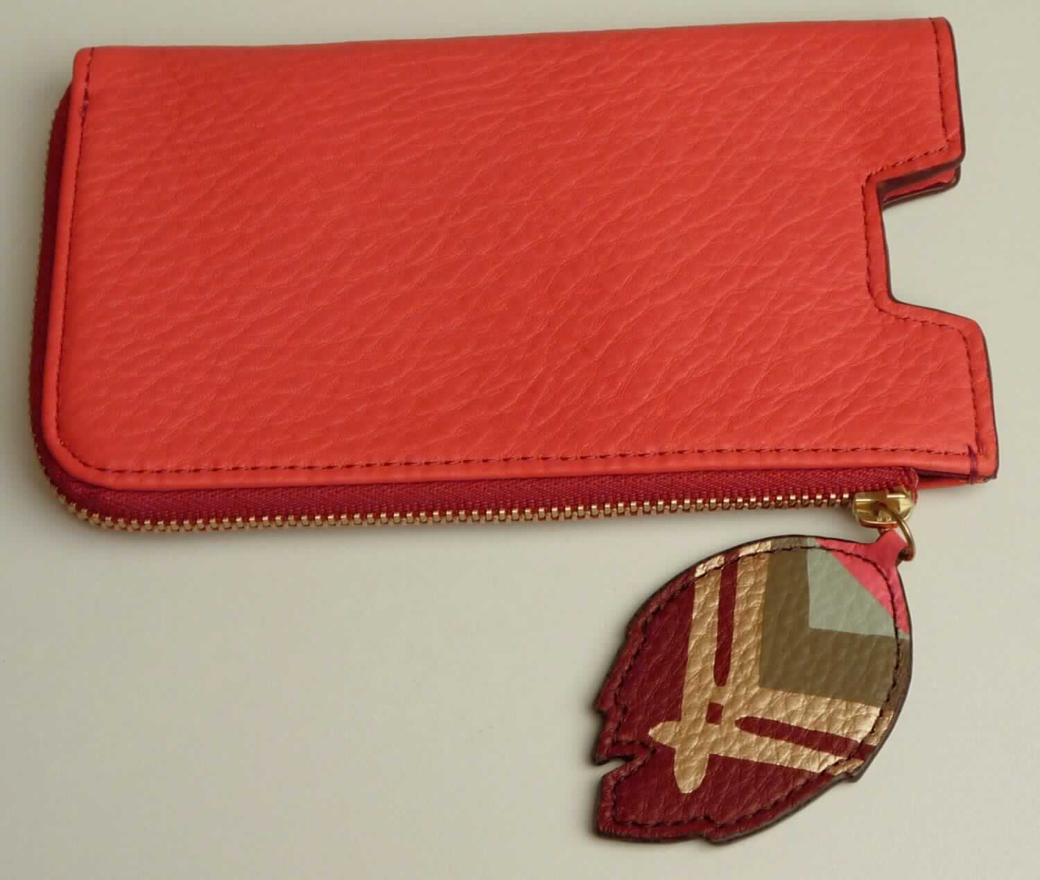 Geldbörse/Etui für ein Mobiltelefon, Taschen- oder Handtaschenartikel, sog. Tech Slide - Color Rose -,
Artikel SL7131652, Foto siehe Anlage, 
- mit einer Außenseite aus Leder (laut Untersuchungsergebnis mit sichtbarer Narbenstruktur),
- gleichermaßen als Geldbörse und als Etui für ein Mobiltelefon gearbeitet,
- - eine Seite bildet die Geldbörse, die andere Seite bildet das Etui,
- Geldbörse:
- - mit einem zweiseitig umlaufenden Reißverschluss; mit einem Zipper in Form eines "Blatts" aus Leder,
- - innen gefüttert und mit zwei Einsteckfächern im Kartenformat ausgestattet,
- Etui für ein Mobiltelefon:
- - oben offen und mit einer Aussparung zur Entnahme eines Mobiltelefons ausgestattet,
- in den Abmessungen: ca. 15,5 cm (Höhe) x 9 cm (Breite) x 1,5 cm (Tiefe),
- ohne Hinweise auf Handarbeit.

"Geldbörse/ähnliches Behältnis (Etui für ein Mobiltelefon), Taschen- oder Handtaschenartikel, mit Außen-
 seite aus Leder, nicht handgearbeitet"