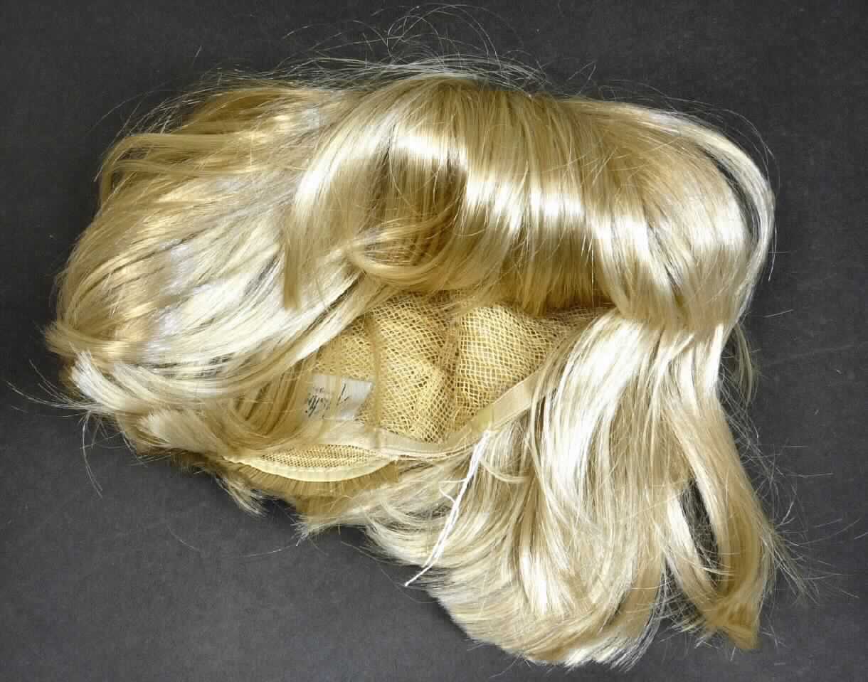 Perücke, Foto siehe Anlage,
- in Form einer vollständigen Perücke,
- aus blond gefärbten, synthetischen Spinnstoffen (lt. Antrag aus Kanekalonfasern), die auf einen
  Unterbau (sog. Montur) aufgenäht sind,
- mit einem Durchmesser von ca. 18 cm.

"Vollständige Perücke, aus synthetischen Spinnstoffen"