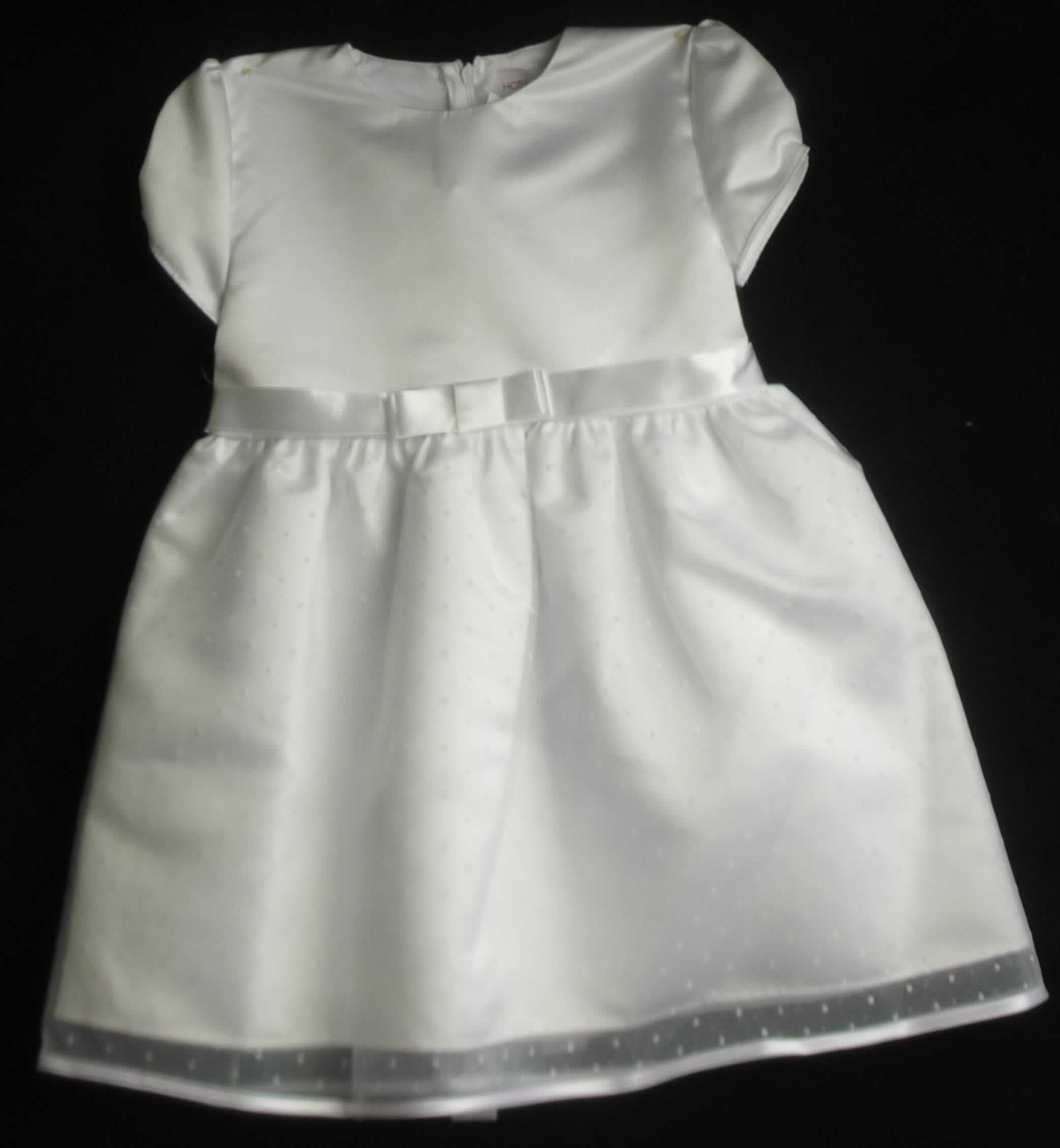 Kleid, sog. Taufkleid, Modell Emilia, Größe 98, Foto siehe Anlage,
- mit einem Oberteil aus ca. 0,5 mm dicken, einfarbigen Geweben und einem dreilagig gearbeiteten Rockteil, mit
  zwei äußeren Lagen aus ca. 0,2 mm dicken, einfarbigen Gewirken und einer inneren Lage aus den Geweben
  des Oberteils; beide Flächenerzeugnisse aus laut Antrag 100 % Polyester (synthetische Chemiefasern),
- im Bereich des Oberkörpers und im Rockteil leicht gefüttert,
- über die Knie reichend (Rückenlänge: ca. 60 cm), 
- mit einem runden Halsausschnitt, 
- hinten mit einer teilweisen, bis in den Rockteil reichenden Öffnung mit Reißverschluss,
- mit kurzen Ärmeln, 
- in Taillenhöhe mit einem Band aus Geweben, das vorn zu einer Schleife gelegt und dann festgenäht ist bzw.
  hinten gebunden werden kann,
- am unteren Rand durch Umschlagen und Festnähen gesäumt bzw. mit einem Band aus den o. a. Geweben
  eingefasst, 
- kann ohne ein weiteres den Unterkörper bedeckendes Kleidungsstück getragen werden,
- ist nicht für Kleinkinder mit einer Körpergröße von bis zu 86 cm bestimmt, damit keine Ware für Kleinkinder,
- im Hinblick auf das äußere Erscheinungsbild sind die Gewirke und die Gewebe als annähernd gleich zu
  betrachten, im Hinblick auf den Umfang jedoch verleihen die Gewirke der Ware ihren wesentlichen Charakter.

"Kleid, aus Gewirken, für Mädchen, aus synthetischen Chemiefasern"