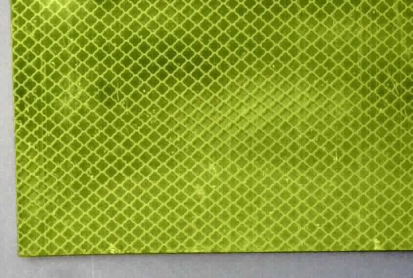 Angaben des Antragstellers:
Selbstklebende, reflektierende Folie mit regelmäßigem Wabenstrukturmuster, bestehend aus einer Acrylpolymerfolie, gefolgt von einer Schicht Poly(methylmethacrylat) mit Mikroprismen, fluoreszierenden Pigmenten sowie einer Schutzfolie.
In Rollen mit einer Breite ab 200 mm bis zu 1240 mm und einer Länge bis maximal 100 m.
Auch in segmentierten Größen und Stücken.

Untersuchungsergebnis an einem Warenmuster (Ergebnisse aus dem Jahr 2012):
Rechteckige, neongelbe, einseitig selbstklebende, reflektierende Folie mit einem regelmäßigen Rautenmuster (siehe Abbildung). Die Folie besteht aus einer gelben Kunststofflage, einer Prismenlage, einer weißen Kunststofflage, einer Klebeschicht und einer klarsichtigen, transparenten Kunststoffschutzfolie (Dicke (ohne Schutzfolie): ca. 0,41 mm).
Auf der Folie befindet sich mehrfach die Kennzeichnung "KWP".

Befund:
Es liegt eine selbstklebende Kunststofffolie der Position 3919 vor.