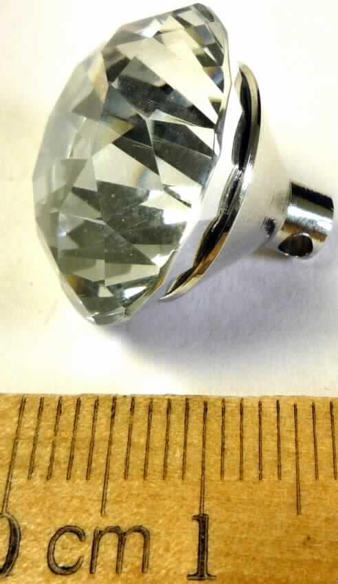 Knopf für Möbel, siehe Foto.
Es handelt sich um einen ca. 1,7 cm großen Knopf, bestehend aus einer kegelförmigen Fassung aus unedlem Metall, mit runder Öse zur Befestigung und einem runden, im Durchmesser ca. 2 cm großen, facettierten Glaskörper im Diamantenschliff.
Charakterbestimmender Stoff nach Umfang und in Bezug auf die Zierwirkung ist das Glas.
Der Knopf ist lt. Antragsangaben zur Verwendung für Möbel bestimmt.
Das Erzeugnis ist als "Knopf, anderer als Druckknopf, aus Glas" einzureihen.