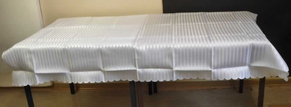 Tischwäsche (Tischdecke), sog. Tischdecke mit gewelltem Rand, Foto siehe Anlage,
- aus ca. 0,2 mm dicken, einfarbigen Geweben aus lt. Antrag 100 % Polyester (synthetische Chemiefasern),
- rechteckig; laut Antrag in den Abmessungen von 132 cm x 178 cm,
- an den Rändern wellenförmig heiß geschnitten (somit konfektioniert),
- wird üblicherweise gewaschen und kennzeichnet sich insbesondere aufgrund des Materials und des 
  Verwendungszwecks als Tischwäsche,
- in einem Polybeutel für den Einzelverkauf aufgemacht.

"Tischwäsche, aus Spinnstoffen, aus Geweben, aus Chemiefasern"