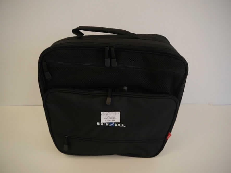 Warenzusammenstellung aus einem handkofferähnlichen Behältnis und einer Regenhülle, sog. Tasche, 
Art.-Nr. 0261UNI (vorgelegtes Warenmuster), Foto siehe Anlage, 
in Aufmachung für den Einzelverkauf, zur Befriedigung eines speziellen Bedarfs zusammengestellt, bestehend aus
- einem handkofferähnlichen Behältnis,
- - mit einer Außenseite aus Spinnstoffen,
- - mit einem verstellbaren, abnehmbaren Schultertragegurt,
- - mit einem gepolsterten Tragegriff,
- - mit zwei Standfüßen aus Kunststoff,
- - mit einem aufgesetzten Vorfach mit Reißverschluss und zwei Reißverschlussfächern auf dem Deckelteil,
- - Hauptfach mit einem an drei Seiten umlaufenden Reißverschluss,
- - an der Innenseite des aufklappbaren Deckels mit einem Einsteckfach ausgestattet,
- - an der Rückseite mit einem Haltesystem aus Kunststoff zur Befestigung am Gepäckträger eines Fahrrads,
- - formstabil durch eingearbeitete Verstärkungen aus Kunststoff,
- - mit den Abmessungen von ca. 40 (L) x 15 (B) x 35 (H) cm, 
- - ohne Hinweise auf Handarbeit,
- einer konfektionierten Spinnstoffware, Regenhülle, 
- - entsprechend der Taschenform zugeschnitten und zusammengenäht (konfektioniert), 
- - an den Rändern mit einem elastischen Zugband ausgestattet, 
- das handkofferähnliche Behältnis bestimmt aufgrund des Umfangs und im Hinblick auf die Verwendung 
  den wesentlichen Charakter der Warenzusammenstellung.

"Handkofferähnliches Behältnis, mit Außenseite aus Spinnstoffen, nicht handgearbeitet"