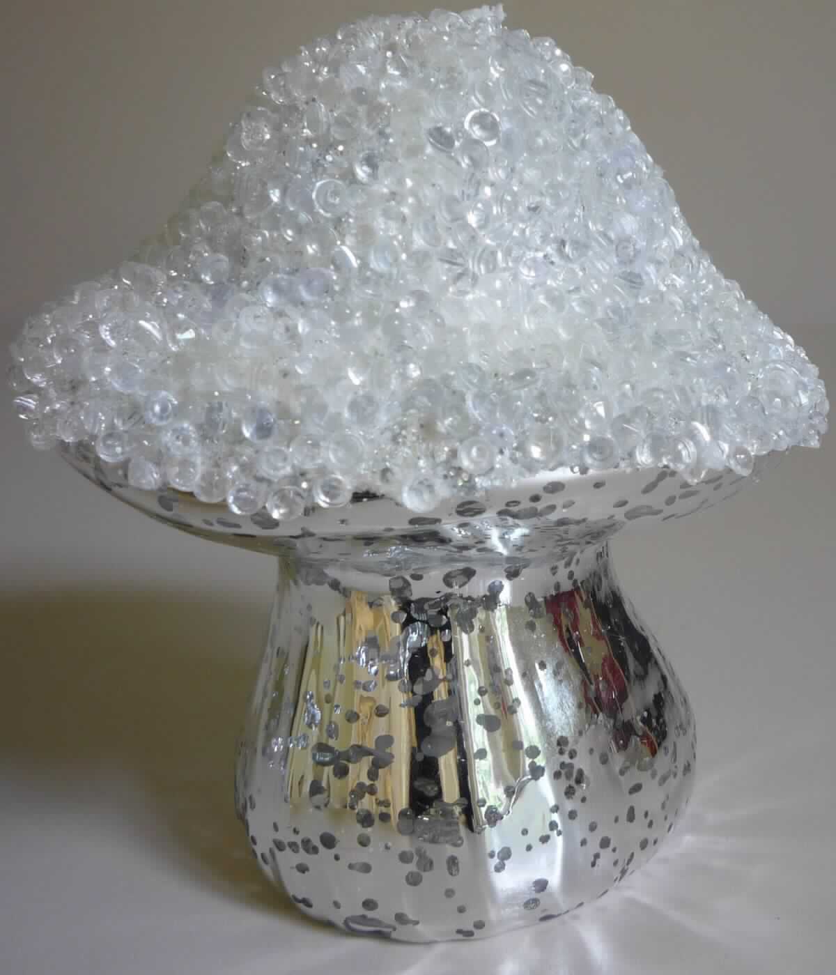 Glasware zur Innenausstattung, sog. LED Glas Pilz, NAN3184179, Foto siehe Anlage,
- aus verschiedenen Bestandteilen zusammengesetzte Ware; bestehend aus: 
- - einer Glasware zur Innenausstattung:
- - - in Form eines innen hohlen Pilzes aus laut Antrag handgefertigtem Borosilikatglas, der im Bereich 
      der Kappe mit kleinen Kügelchen aus Kunststoff verziert ist (das Glas ist im Hinblick auf den Umfang
      und die Formgebung charakterbestimmend),
- - - innen teilweise (besprenkelt) verspiegelt, 
- - einem elektrischen Beleuchtungskörper: 
- - - mit zwei Leuchtdioden (LED),
- - - batteriebetrieben; mit einem integrierten Batteriefach mit einem Ein-/Aus-Schalter,
- - - die Beleuchtung dient lediglich der Erhöhung der Zierwirkung des Pilzes,
- die Glasware bestimmt im Hinblick auf die Verwendung der zusammengesetzte Ware 
  als Ziergegenstand deren wesentlichen Charakter,
- verpackt in einer bedruckten Pappschachtel.

"Glasware zur Innenausstattung, andere als solche aus Glaskeramik oder aus Bleikristall, handgefertigt"