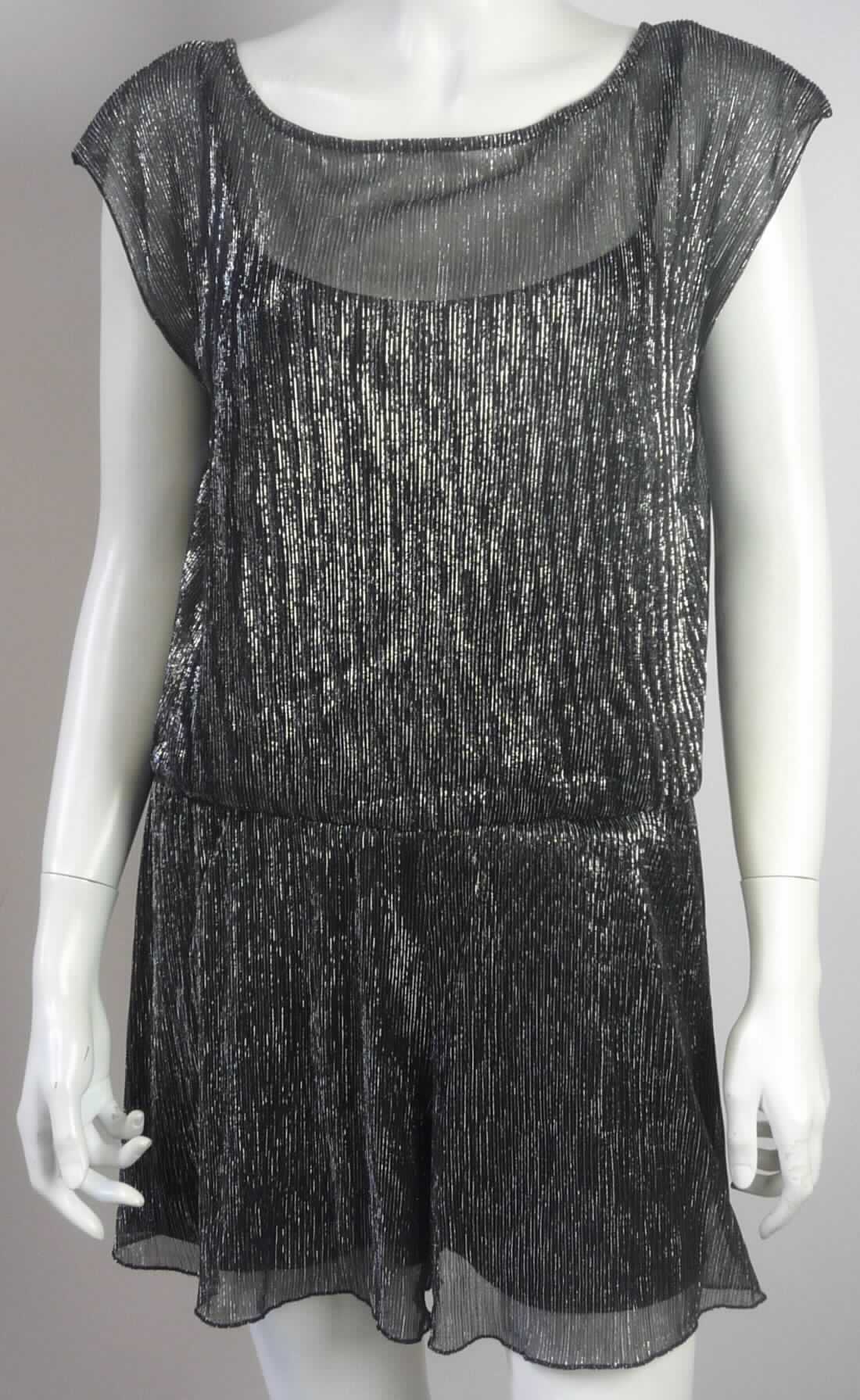 Hosenrockkleid, sog. Damenoverall, Art. 6403897.00.71, Größe S, Foto siehe Anlage,
- doppellagig gearbeitet, mit einer Außenlage aus ca. 0,5 mm dicken, buntgewirkten Gewirken aus laut Antrag 
  55 % metallisierten Garnen (metallisierte Streifen aus synthetischer Spinnmasse) und 45 % Polyester 
  (synthetische Chemiefasern) und einer Innenlage aus ca. 0,4 mm dicken, einfarbigen Gewirken aus 
  augenscheinlich Chemiefasern; beide Lagen sind an den Schultern und in der Taille dauerhaft zusammengenäht,
- vorn mit einem runden, im Rücken mit einem V-förmigen Ausschnitt,
- ohne Öffnung und ohne Verschluss,
- mit sehr kurzen Ärmeln,
- im Taillenbereich mit einer elastischen Verengung,
- mit sehr weiten, kurzen Hosenbeinen (Seitenlänge: ca. 32 cm), die dem Kleidungsstück aufgrund der Schnittform 
  den optischen Eindruck eines Kleides und damit den Charakter eines Hosenrockkleides verleihen (somit kein 
  Overall),
- am unteren Rand durch Überwendlichnähte (Außenlage) bzw. durch Umschlagen und Festnähen (Innenlage)
  gesäumt,
- im Hinblick auf das äußere Erscheinungsbild und den Umfang überwiegend die buntgewirkten Gewirke, sie bilden
  damit das für die Spinnstoffermittlung maßgebende Flächenerzeugnis.

"Hosenrockkleid, aus Gewirken, für Frauen, andere als in den Unterpositionen 6104 41 bis 6104 44 genannte"