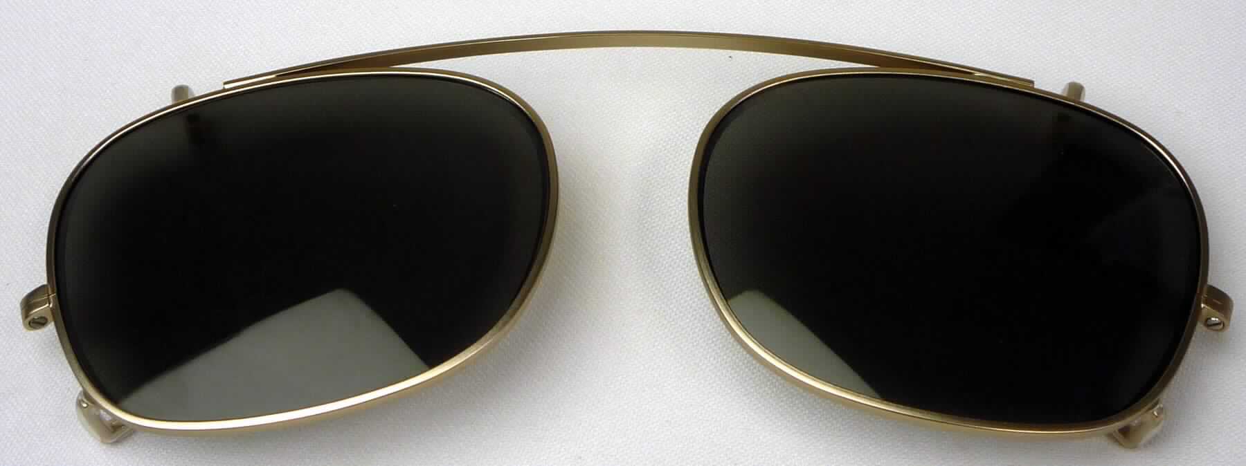 Sog. Teile für Brillenfassungen mit nicht bearbeiteten Kunststoffsonnengläsern, in Form von getönten Brillengläsern aus Kunststoff in einer Brillenfassung aus Metall, ohne Bügel, mit seitlichen Ösen und einer Clip-Vorrichtung zum Aufstecken auf eine Brille als Schutz vor UV-Strahlung durch die Sonne.
Zur äußeren Form siehe Abbildung in Anlage.

Die Ware wird als "brillenähnliche Ware, andere als Sonnenbrille, mit Brillengläsern aus Kunststoff" eingereiht.