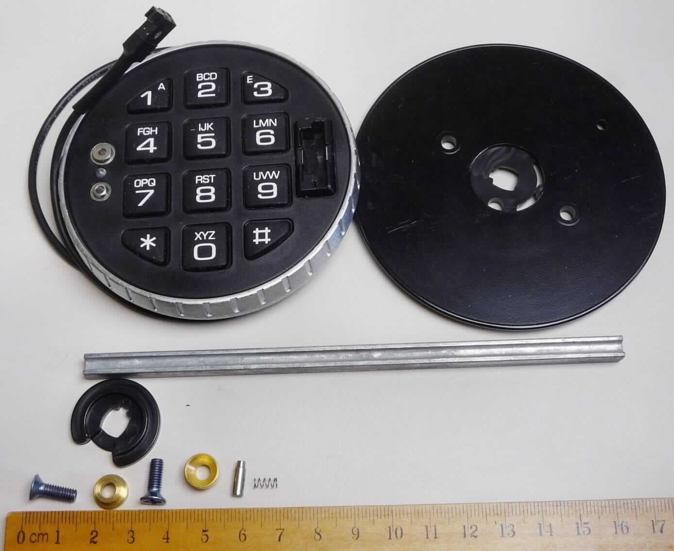 Bedieneinheit für elektronische Tresorschlösser.
Das scheibenförmige Erzeugnis (Durchmesser etwa 9,5 cm, Höhe etwa 2,0 cm) besteht aus einem Korpus und einer Grundplatte aus unedlen Metallen. Die im Druckgussverfahren hergestellten Teile weisen spezifisch geformte Aussparungen bzw. Durchbohrungen für die Montage der Bedieneinheit auf an die Außenseite einer Tresortür auf. In den Korpus eingesetzt ist eine mit elektronischen (u.a. EEPROM, Signal-LED) und anderen Bauelementen (u.a. ein akustischer Signalgeber, mehrere Widerstände) bestückte gedruckte Schaltung. An der Leiterplatte angebracht ist ein Rundkabel mit 4-poliger Buchse zur elektrischen Verbindung der Bedieneinheit mit einem Tresorschloss (nicht Gegenstand dieser vZTA). Auf die Leiterplatte aufgesetzt ist eine flexible Tastatur aus Kautschuk mit 12 Funktions- und Zifferntasten, die frontseitig mit einem Raster aus Kunststoff abgedeckt ist. Des Weiteren ist das Bedienfeld mit einem Schnittstellenstecker zum Einstecken eines elektronischen Code-Schlüssels sowie zwei Kontakten zur Notstromversorgung des Batterieblocks (nicht Gegenstand dieser vZTA) ausgestattet.
Die Bedieneinheit ist gemeinsam verpackt mit einer Spindel in Gestalt einer Profilstange aus unedlem Metall, um Grundplatte und Korpus der Bedieneinheit mit dem Tresorschloss formschlüssig zu verbinden. Das beigepackte Montagematerial besteht aus je zwei Senkkopfschrauben und  Ansatzbuchsen, einem Arretierstift und einer Schraubenfeder aus unedlen Metallen sowie einer spezifisch geformten Lagerscheibe aus Kunststoff. 
Das Erzeugnis dient nach Eingabe des passenden Geheimcodes zum Freigeben oder Blockieren des Riegelwerks eines Tresorschlosses (nicht Gegenstand dieser vZTA) bzw. zum Verwalten des Geheimcodes (Anlegen, Löschen, Aktivieren und Deaktivieren).
Die Anteile aus unedlen Metallen bestimmen wegen ihres Umfangs den Charakter der aus verschiedenen Stoffen zusammengesetzten Ware.

Abbildung siehe Anlage.

Derartige Erzeugnisse gehören als "Teile aus unedlen Metallen für Schlösser (elektrische Schlösser) aus unedlen Metallen" zum TARIC-Code 8301 6000 90.
