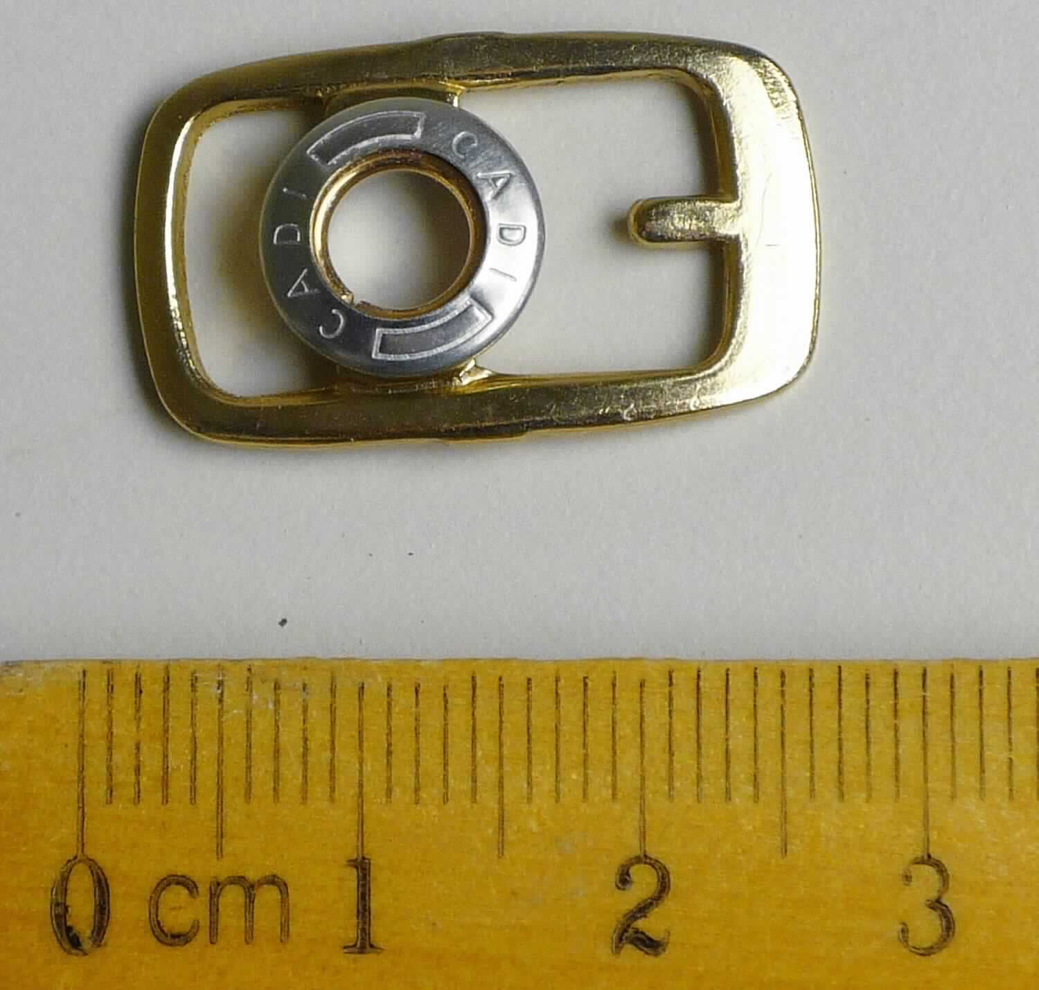 Bei der aus gewalztem Stahl bestehenden Schnalle mit abgerundeten Ecken (Breite ca. 15 mm und Länge ca. 25 mm) handelt es sich um ein erkennbares Teil eines Druckknopfs, der als Schuhverschluss eingesetzt wird.

Die Ware wird als erkennbares Teil eines Druckknopfs eingereiht.