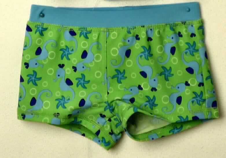 Zweiteilige Zusammenstellung, bestehend aus einem modischen Unterhemd und einer Badehose, sog. Sonnenschutz-Badeset für Kinder, Größe 98/104, Foto siehe Anlage,
- mit einem Polystring verbunden und zusammen für den Einzelverkauf aufgemacht,
- aus ca. 0,6 mm dicken, einfarbigen und bedruckten Gewirken aus lt. Antrag 80 % Polyamid und 20 % Elasthan 
  (Elastomergarn; beides synthetische Chemiefasern); ohne Kautschukfäden, die Elastizität ergibt sich durch die 
  Verwendung von Elastomergarnen,
- kein zweiteiliger Badeanzug, u. a. da das Oberteil aufgrund seiner Beschaffenheit (Schnitt und Ausstattung) 
  nicht erkennen lässt, dass es ausschließlich oder hauptsächlich dazu bestimmt ist, als Badekleidung getragen 
  zu werden,
- keine Kombination, u. a. weil sowohl Badehosen der Position 6112 als auch modische Unterhemden der 
  Position 6109 nicht als Bestandteil einer Kombination zugelassen sind,
- Badehose:
-- in der Taille abschließend, mit einem angesetzten, elastischen Bund,
-- ohne Öffnung und ohne Verschluss,
-- im vorderen Bereich mit einem Gewirke unterlegt (Hygieneeinlage); aufgrund der Ausstattung erkennbar 
   Knabenkleidung,
-- mit kurzen, gerade geschnittenen Hosenbeinen,
-- an den Beinabschlüssen durch Umschlagen und Festnähen gesäumt,
-- die Hose lässt nach Schnitt, Material und Ausstattung erkennen, dass sie ausschließlich oder hauptsächlich
   dazu bestimmt ist, als Badekleidung getragen zu werden.

"Badehose, aus Gewirken, für Knaben, aus synthetischen Chemiefasern, keine Kautschukfäden enthaltend"