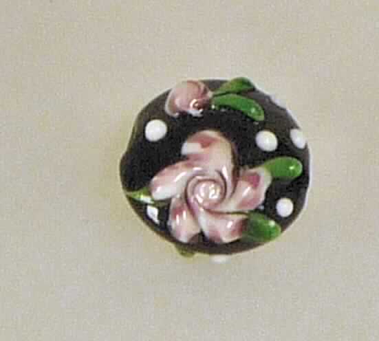 Glasperlen, sog. Schmuck/Perle, Art. 337099, Foto siehe Anlage, 
- ovale, steinförmige Erzeugnisse aus lt. Antrag Glas,
- mit einer schwarzen, glatten Grundfläche und leicht erhabenen Nachbildungen von Blüten und
  weißen Punkten,
- entlang der Mittelache vollständig durchbohrt, 
- mit einem Durchmesser von ca. 2 cm und einer Dicke von ca. 2 cm,
- u. a. an den Außenseiten ohne scharfkantige Schleifflächen, die Waren stellen sich daher nicht
  als geschliffen und mechanisch poliert dar,
- ohne Hinweise auf Handarbeit,
- keine Nachahmungen von Perlen,
- keine Nachahmungen von Edel- oder Schmucksteinen,
- dienen zu Schmuckzwecken.

"Glasperlen, nicht geschliffen und mechanisch poliert, nicht handgearbeitet"