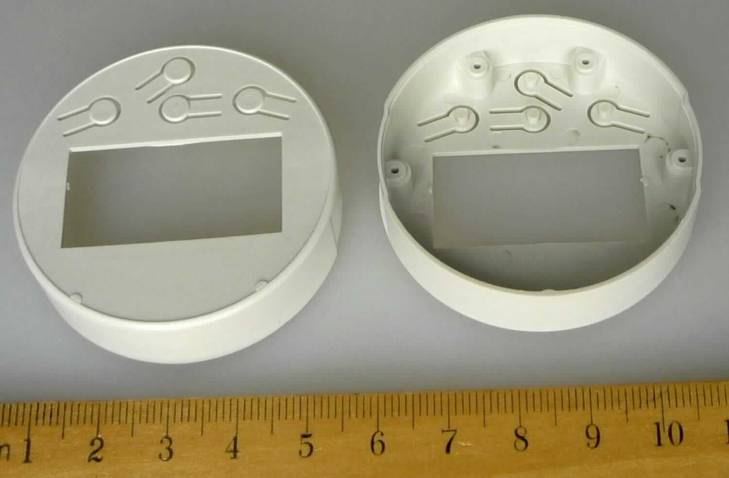 Gehäuse für Messgerät, im Wesentlichen bestehend aus einem Kunststoff mit dem Durchmesser von ca. 49 mm und der Höhe von ca. 12 mm.
Die Ware weist die Form einer Schale auf, deren Rand vollständig rechtwinklig in eine Richtung gebogen ist. Die ebene Oberfläche ist mittig von einem Rechteck mit den Abmessungen von ca. 33 x 14 mm durchbrochen. Unterhalb des Rechtecks sind 4 Ausstanzungen mit einer Länge von jeweils ca. 10 mm erkennbar, die fingerförmige Gebilde erkennen lassen und der Aufnahme von Tastelementen dienen.
Auf dem Rand sind in Höhe des Rechtecks, links und rechts von diesem, 2 fingerbreite geringe Vertiefungen vorhanden.
Im Innern des Gehäuses sind 4 Verdickungen erkennbar, die sich neben und unterhalb der rechteckigen Aussparung befinden, die mutmaßlich Befestigungszwecken dienen.
Die Ware wird als Gehäuseteil in verschiedene Geräte zum Messen und Kontrollieren von Druck, Durchfluss, Temperatur, und anderen Parametern bei Flüssigkeiten und Gasen eingebaut.

Zur äußeren Form siehe Abbildung in der Anlage.

Die Ware wird als "Teil für Geräte des Kapitel 90, in Kapitel 90 anderweit weder genannt noch inbegriffen, nicht von der Unterposition (TARIC) 9033 0010 00 erfasst" eingereiht.