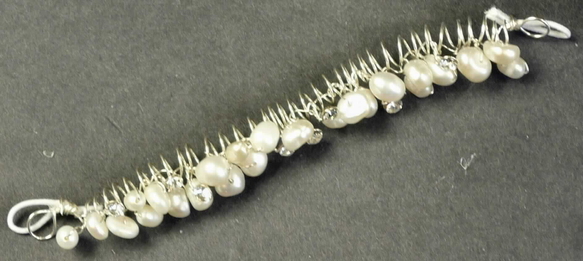 Es handelt sich um etwa 11 cm lange sog. Schleierabschlüsse, bestehend aus Süßwasserperlen und Straßsteinchen, die mittels Draht aus unedlem Metall an einem spiralförmigen Draht aus unedlem Metall befestigt sind. Die beiden Enden sind zu Ösen ausgearbeitet und mit einem elastischen Band versehen. 
Die Erzeugnisse sind in einem Kunststoffbeutel verpackt.
- lt. Antragstellerangaben - 

Abbildung siehe Anlage.

Derartige Erzeugnisse gehören als "Waren aus echten Perlen oder Zuchtperlen" zum TARIC-Code 7116 1000 00.