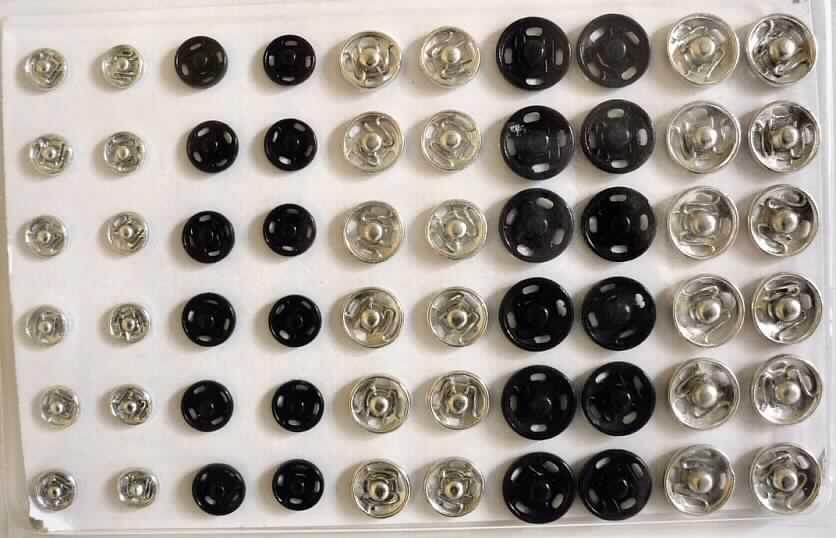 Set mit Druckknöpfen (Artikel 288219, siehe Foto) aus unedlem Metall, beinhaltet sechzig Stück, in Schwarz und Silber, drei verschiedene Größen, jeder Knopf besteht aus zwei Teilen (Ober- und Unterteil).
Die Druckknöpfe sind auf einen Streifen aus Pappe gesteckt (8,5 x 13,5 cm) und in einer Sichtverpackung aus klarsichtigem Kunststoff mit Papprücken für den Einzelverkauf aufgemacht.

Die Ware ist als "Drucknöpfe" einzureihen.