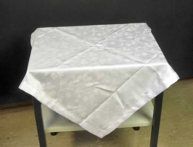 Tischwäsche (Tischdecke), Foto siehe Anlage,
- quadratisch; mit einer Seitenlänge von etwa 80 cm,
- aus 0,5 mm dicken, einfarbigen (weißen) Geweben aus 100% Chemiefasern; mit floralem Muster,
- an den Rändern gesäumt (somit konfektioniert),
- kann als Mitteldecke auf die Mitte des Tischs gelegt werden,
- wird üblicherweise gewaschen und kennzeichnet sich insbesondere aufgrund des
  Materials und der Ausstattung als Tischwäsche.

"Tischwäsche, aus Geweben, aus Chemiefasern"