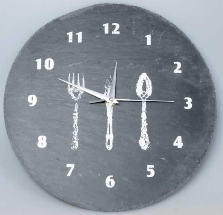 Runde Wanduhr aus Schiefer (Artikel-Nr.: 46697), ca. 30 cm im Durchmesser, mit Kleinuhr-Werk, elektrisch betrieben (Batterie), mit Stunden-, Minuten- und Sekundenzeiger und arabischem Zifferblatt, auf dem ein dreiteiliges Besteck (Gabel, Messer und Löffel) abgebildet ist. Der Einstellknopf für die Uhrzeit, das Batteriefach und eine Aufhängevorrichtung befinden sich auf der Rückseite der Uhr.
Die Uhr ist in einer Sichtbox aus Pappe aufgemacht.

Die Ware ist als Uhr mit Kleinuhr-Werk, elektrisch betrieben, einzureihen.