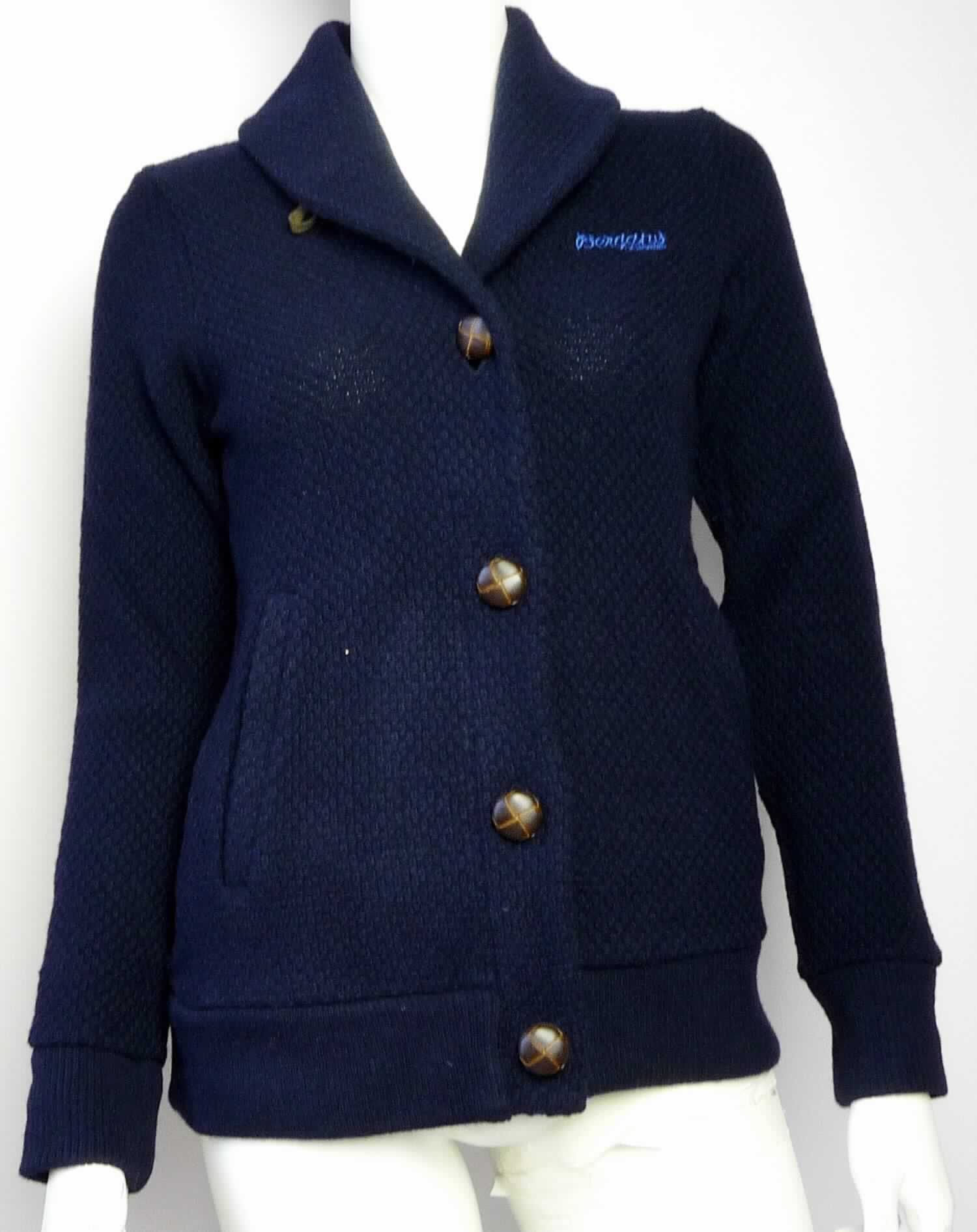Strickjacke, sog. Tepperot Lady Jkt, Art. Nr. 1893, Größe XS, Foto siehe Anlage,
- aus ca. 2,6 mm dicken, strukturiert gewirkten, einfarbigen Gewirken aus laut Antrag 70 % Wolle, 
  25 % Polyamid (synthetische Chemiefasern) und 5 % anderen Fasern, 
- ungefüttert,
- über die Taille reichend (Rückenlänge: ca. 60 cm), 
- mit einem Umlegekragen,
- vorn mit einer durchgehenden Öffnung mit Knopfverschluss von rechts auf links (Frauenkleidung), 
- mit langen Ärmeln,
- im Brustbereich mit einer Stickerei verziert,
- vorn mit zwei eingesetzten, offenen Taschen unterhalb der Taille,
- am unteren Rand mit einem angesetzten, nicht verengenden Bund,
- weist weder aufgrund der Ausstattung (ungefüttert) noch des Schnitts (nicht in Bahnen gearbeitet) 
  eine Formfestigkeit auf, somit keine Jacke,
- wird im Allgemeinen nicht über jeder anderen Kleidung und zum Schutz gegen das Wetter getragen, 
  somit keine Ware der Position 6102.

"Strickjacke, aus Gewirken, aus Wolle, für Frauen"