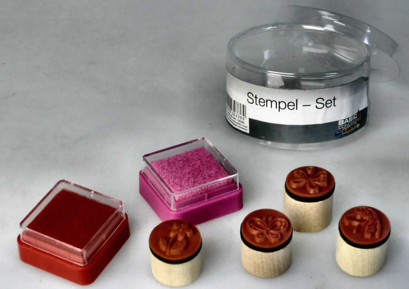 Feuchtstempel für den Handgebrauch, als Warenzusammenstellung in Aufmachung für den Einzelverkauf, sog. Stempel-Set, bestehend aus 4 Stempeln und 2 mit roter und rosaner Farbe getränkten Stempelkissen in ca. 3 cm x 3 cm x 1,5 cm (Länge x Breite x Höhe) großen Kunststoffkästchen. Die Stempel bestimmen im Hinblick auf den Umfang und die Bedeutung für die Verwendung den Charakter der Warenzusammenstellung und bestehen aus runden, ca. 1,5 cm hohen und im Durchmesser ca. 2 cm großen Holzklötzen, jeweils beklebt mit einer schwarzen Schaumstoffschicht (für einen weichen Stempelabdruck), auf der sich eine Gummifläche mit einem Stempelmotiv als Relief (2 verschiedene Schmetterlinge, 1 Pferdekopf und 1 Blume) befindet. 
Die Stempel sind mit den Stempelkissen in einer runden, durchsichtigen Kunststoffschachtel für den Einzelverkauf aufgemacht.

Das Erzeugnis ist als "Stempel, für den Handgebrauch" einzureihen.

Anlage: 1 Abbildung