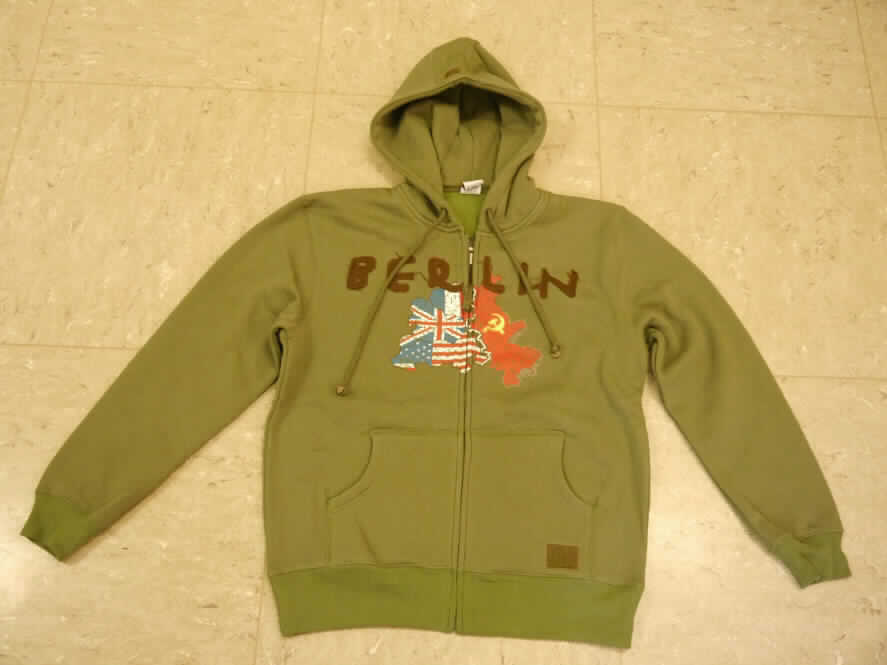 Blouson, sog. Kapuzenjacke, Größe XL, Foto siehe Anlage,
- aus ca. 2,0 mm dicken, einbfarbigen, auf der Innenseite gerauten Gewirken aus laut Antrag 100 % Baumwolle,
- über die Taille reichend (Rückenlänge: ca. 73 cm),
- mit einer angesetzten, doppelt gearbeiteten Kapuze mit Kordelzug,
- vorn mit einer durchgehenden Öffnung mit Reißverschluss,
- ohne Hinweise auf den Trägerkreis (unisex),
- mit langen Ärmeln, die über den unteren Rand des Kleidungsstücks hinausreichen; an den Ärmelenden
  mit angesetzten, gerippt gewirkten, verengenden Bündchen,
- auf der Vorderseite mit einem Aufdruck und einem aufgenähten Schriftzug verziert,
- mit zwei aufgesetzten, offenen Taschen (sog. Kängurutaschen) unterhalb der Taille,
- am unteren Rand mit einem angesetzten, doppelt gearbeiteten, gerippt gewirkten, verengenden Bund.

"Blouson, aus Gewirken, für Frauen, aus Baumwolle"