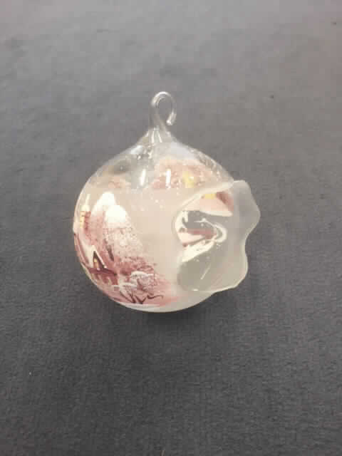Ziergegenstand aus lampengeblasenem (gesponnenem) Glas, sog. Teelichtkugel, TK 177.1, Foto siehe Anlage,
- in Form einer auf einer Seite offen gearbeiteten Kugel aus Glas,
- aus lt. Antrag lampengeblasenem, klarsichtigem Glas, 
- an der Oberseite mit einer angearbeiteten Öse,
- mit einem Durchmesser von ca. 9 cm,
- die Oberseite ist mit einem winterlichen Motiv (u. a. verschneite Landschaft, Häuser und Pferdekutsche)
  bemalt,
- kein Weihnachtsfestartikel der Position 9505, da ein festlicher Bezug nicht vorhanden ist (die Ware ist
  lediglich mit winterlichen und nicht mit weihnachtlichen Motiven verziert),
- keine Einreihung als nicht elektrischer Beleuchtungskörper in die Position 9405, da die Ware weder eine
  passgenaue Vorrichtung für ein handelsübliches Teelicht noch einen Dorn oder eine andere 
  Befestigungsmöglichkeit für eine Kerze aufweist.

"Ziergegenstand aus lampengeblasenem (gesponnenem) Glas, kein Fantasieschmuck"