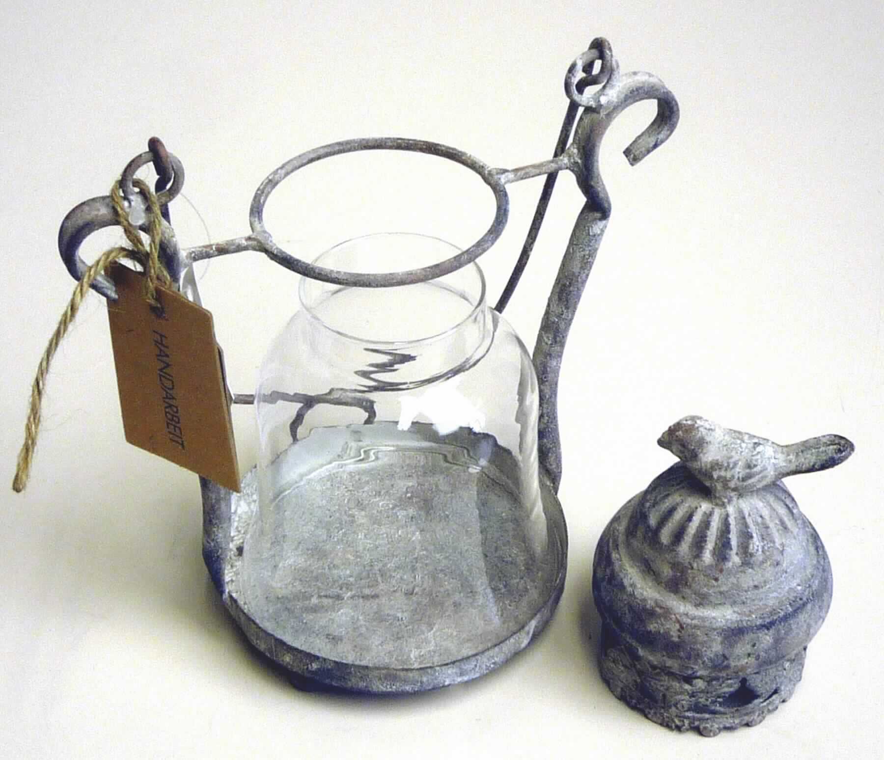 Bei der sog. "Laterne Metall" handelt es sich um einen nicht elektrischen Beleuchtungskörper in Form einer ca. 20 cm hohen, handgearbeiteten (lt. AStin) Laterne mit einem Gestell aus Metall und einem glockenförmigen Glaseinsatz.
Das Gestell besteht im Wesentlichen aus einem kreisförmigen Boden (d: 10,5 cm) mit drei kugelförmigen Füßen und zwei vertikal angebrachten Metallstangen, die am oberen Ende mittels einem Querstab verbunden sind. 
Die Laterne ist mit einem geschlossenen Dach mit Luftabzug zur Abführung von Wärme, sowie einem Tragegriff versehen. Das mit einem stilisierten Vogel verzierte Dach und der Glaseinsatz lassen sich zum Abstellen einer Kerze oder eines Teelichtes abnehmen.

Das Erzeugnis ist mit einem Etikett mit der Beschriftung "HANDARBEIT" versehen und in einem Karton verpackt.

Die Ware ist als "nicht elektrischer Beleuchtungskörper, anderweit weder genannt noch inbegriffen, handgearbeitet" einzureihen.
