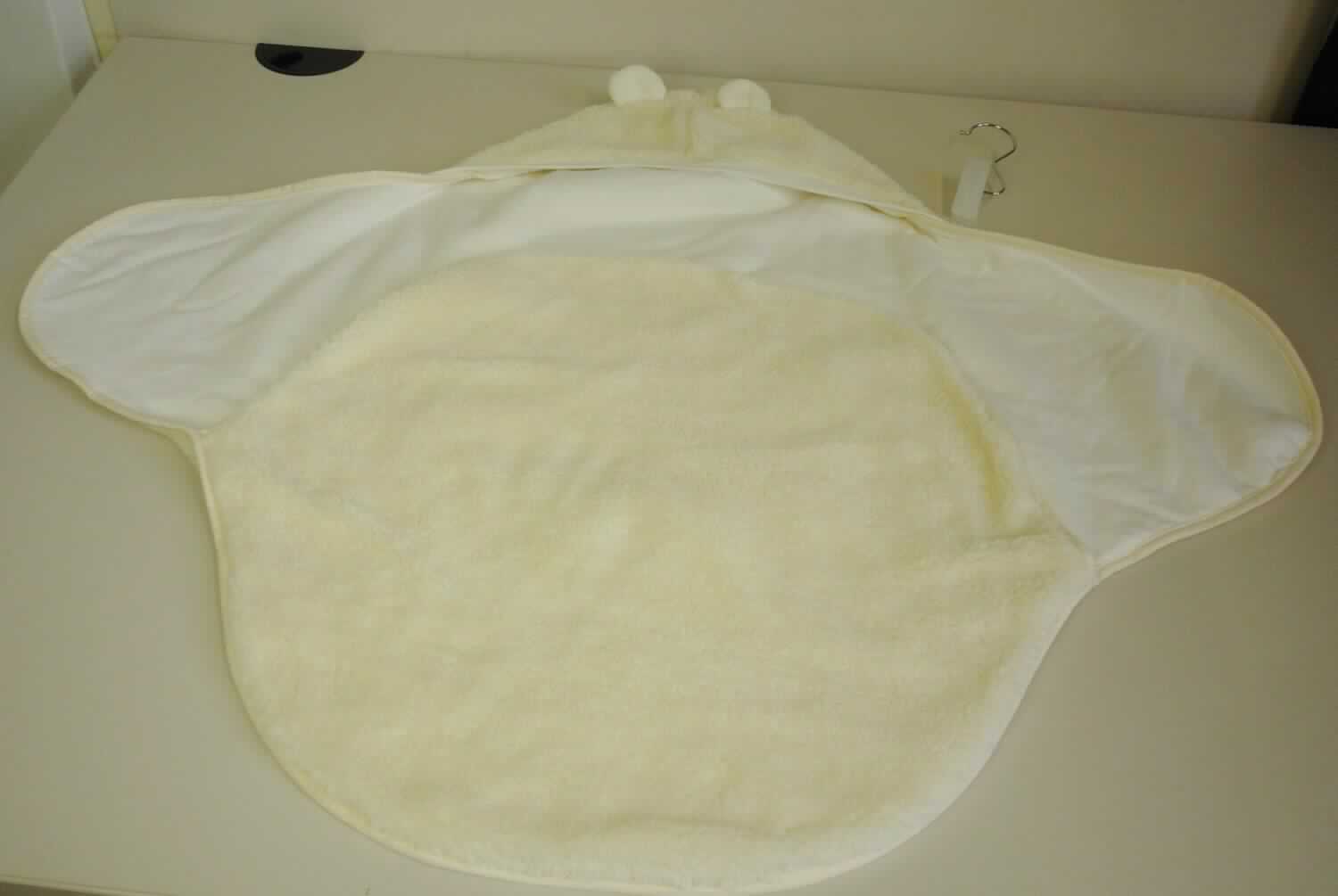 Strampelsackähnliche Ware, sog. Einschlagdecke, Art. Nr. 9031508, Foto siehe Anlage,
- mit einem bedruckten Pappeinleger auf einem Kleiderbügel aufgemacht,
- annähernd rautenförmig, in den Abmessungen von laut Antrag (H x B): 75 cm x 90 cm,
- doppelt gearbeitet, 
-- mit einer Außenseite (Schauseite) aus ca. 5 mm dicken, einfarbigen Plüschgewirken aus laut Antrag 
   100 % Polyester (synthetische Chemiefasern), 
-- mit einer Innenseite aus ca. 0,7 mm dicken, einfarbigen Gewirken aus laut Antrag 100 % Baumwolle,
- an einer Ecke mit einer Kapuze mit stilisierten "Ohren", 
- im Bereich des Oberkörpers mit Seitenteilen, die übereinander geschlagen werden, im unteren Teil in der 
  Art eines Strampelsackes gearbeitet,
- auf der Rückseite mit einer ca. 8 cm langen Öffnung, durch die ein Drei-Punkt-Gurt, z. B. eines Autositzes, 
  einer Babyschale oder eines Kinderwagens, gezogen werden kann,
- an den Rändern mit Gewebebändern eingefasst,
- stellt sich aufgrund der Ausstattung nicht als Decke dar,
- ist aufgrund der Abmessungen für Kleinkinder mit einer Körpergröße von bis zu 86 cm bestimmt,
- insbesondere im Hinblick auf das äußere Erscheinungsbild ist das Gewirke aus synthetischen Chemiefasern
  das für die Spinnstoffermittlung maßgebende Flächenerzeugnis.

"Kleidung aus Gewirken (Strampelsackähnliche Ware), für Kleinkinder, aus synthetischen Chemiefasern"