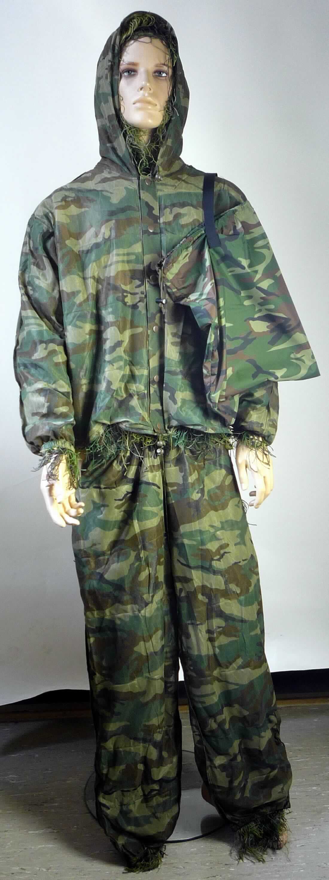 Zweiteilige Zusammenstellung, bestehend aus einem Blouson und einer langen Hose, sog. Ghillie Suit, 
Art. 1196...., Größe M/L, Fotos siehe Anlage,
- gemeinsam in einem einfachen Spinnstoffbeutel für den Einzelverkauf aufgemacht (übliche Verpackung im Sinne 
  der Anmerkung 5 b)),
- aus ca. 0,3 mm dicken, in Tarnfarbenoptik bedruckten Gewirken aus laut Antrag 100 % Polyester 
  (synthetische Chemiefasern), auf die in regelmäßigen Abständen Bündel aus verschiedenfarbigen Garnen
  aus laut Antrag 100 % Polypropylen (synthetische Chemiefasern) aufgenäht sind,   
- keine Kombination, weil die aufgenähten Garnbündel nicht als zulässige Verzierungen gelten, da sie außer einer 
  Zierwirkung auch noch eine weitere Funktion (Tarneffekt) aufweisen, 
- aufgrund der Ausstattung und der Verwendung kein Trainingsanzug,  
- erfüllt die Voraussetzung zur Einreihung als Kleidung in das Kapitel 61, somit keine Ware der Position 6307
- Blouson:
-- über die Taille reichend (Rückenlänge: ca. 63 cm),
-- mit einer angenähten Kapuze mit Kordelzug, 
-- vorn mit einer durchgehenden Öffnung mit Druckknopfverschluss von links über rechts (Männerkleidung),
-- mit langen Ärmeln, die über den unteren Rand des Kleidungsstücks hinausreichen; an den Ärmelenden mit
   verengenden Abschlüssen,
-- am unteren Rand mit einem Tunnelzug zu verengen,
-- erfüllt die Merkmale zur Einreihung als Blouson, somit keine Jacke.

"Blouson aus Gewirken, für Männer, aus Chemiefasern"
