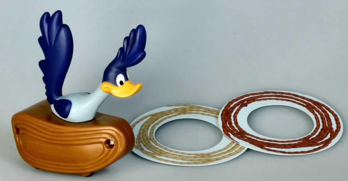 Bei dem Motiv "Road Runner Lasso" der Aktion "Mc Donald's - Active Play 2010" handelt es sich um ein mit vier beweglichen Rädern und einem Rückziehmotor ausgestattetes, mehrteiliges Ringwurfspiel aus Kunststoff (charakterbestimmend aufgrund des Umfangs) und Pappe, bestehend aus
- einem Fantasiefahrzeug, auf dem die Gestalt der Cartoon-Figur "Road Runner", einem flugunfähigen und rasend schnell laufenden Vogel, fixiert ist, und
- zwei Pappringen/-scheiben mit einem Außendurchmesser von ca. 8 cm und einem Innendurchmesser von ca. 4,3 cm.
Die Pappscheiben sind mit Lassomotiven bedruckt und sollen in der Bewegung über die Figur geworfen werden.

Das Erzeugnis dient der spielerischen Unterhaltung von Kindern und ist mit einem Beipackzettel in einem Polyethylenbeutel verpackt. 

Die Ware ist als "anderes als zuvor von der Position 9503 erfasstes Spielzeug mit eingebautem Motor, aus Kunststoff" einzureihen
