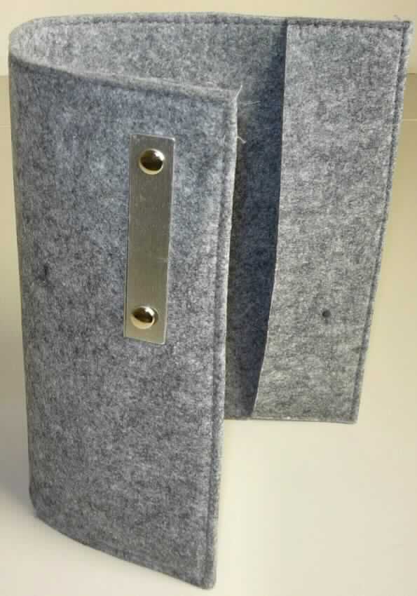 Buchhülle, sog. Notizbuchetui "Filz" A4, Art. 06991012-00000, Foto siehe Anlage,
- annähernd rechteckig; flachliegend in den Abmessungen von ca. 44 cm x 31 cm,
- laut Untersuchungsergebnis:
-- aus Nadelfilz aus Spinnstoffen,  
- an den Enden in der Länge von ca. 6,5 cm nach innen umgeschlagen und an den Längsseiten so 
  zusammengenäht, dass zwei Laschen zum Einschieben der Einbände von Büchern entstehen, 
- mit einem durch Nieten angebrachten Plättchen aus unedlem Metall (ca. 8 cm x 2,5 cm) verziert,
- durch Zusammennähen konfektioniert.

"Andere konfektionierte Ware (Notizbuchetui), aus Spinnstoffen, aus Filz"