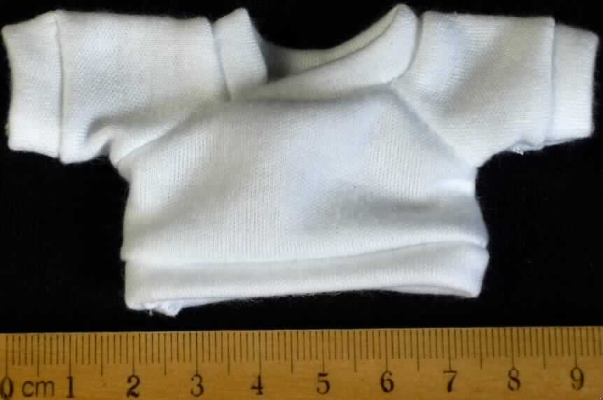 Es handelt sich um ein ca. 5 x 9,5 cm (HxB; Breite mit Ärmeln) großes, weißes T-Shirt aus Spinnstoff mit einem runden Halsausschnitt und kurzen Ärmeln. Der Kragenbereich, die Ärmelenden und der gerade, untere Rand des Shirts sind mit einem Bund ausgestattet.

Das T-Shirt ist aufgrund der Gestaltung erkennbar hauptsächlich als Zubehör für Puppen bestimmt. Eine mögliche Verwendung als Zubehör für Plüschtiere steht der Einreihung nicht entgegen. 

Die Ware dient der spielerischen Unterhaltung von Kindern mit Puppen.

Das Erzeugnis ist als "Zubehör für Puppen, nur Nachbildungen von Menschen darstellend" einzureihen.